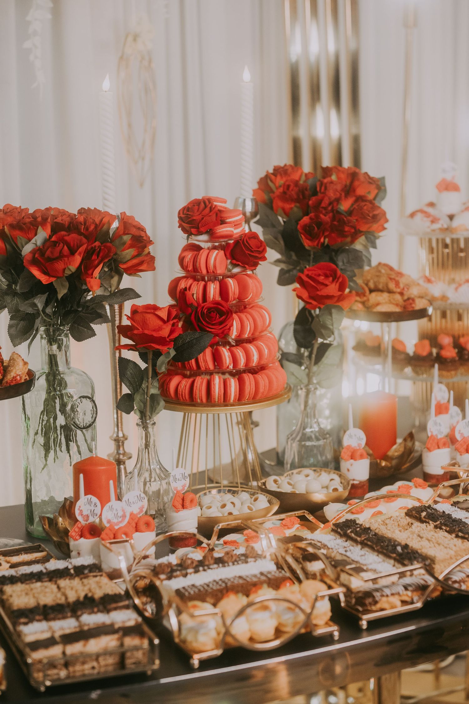 Red macaron tower surrounded by red roses, candles, and assorted desserts on a wedding candy bar. Epicu Fotograf Drobeta-Turnu Severin