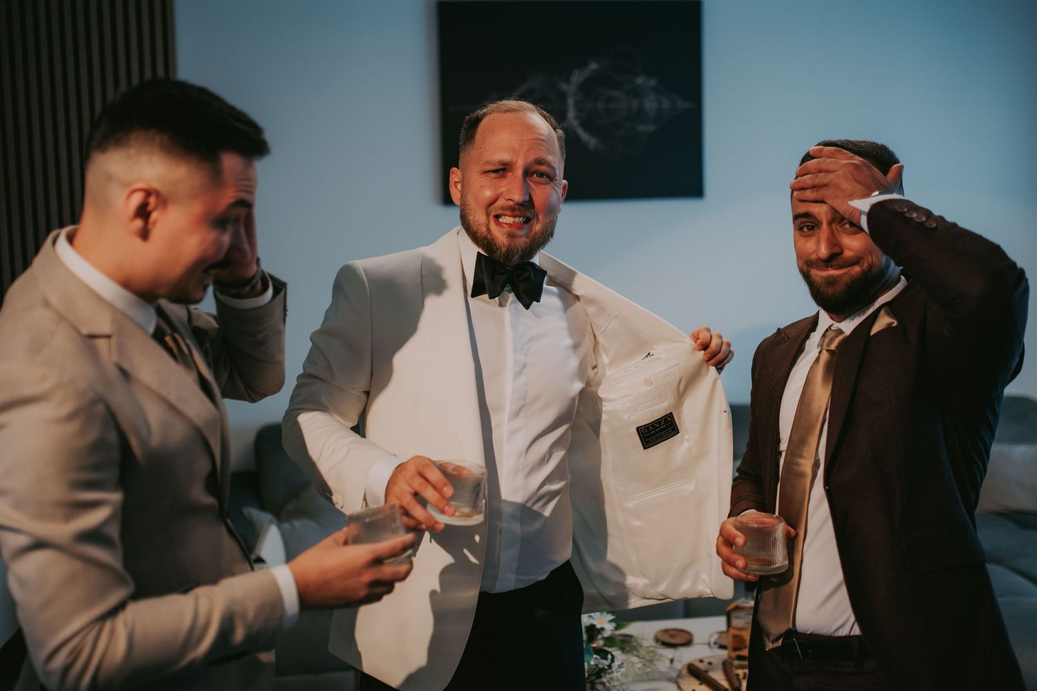 Groom in white tuxedo laughing and celebrating with groomsmen holding drinks at wedding. Epicu Fotograf Drobeta-Turnu Severin