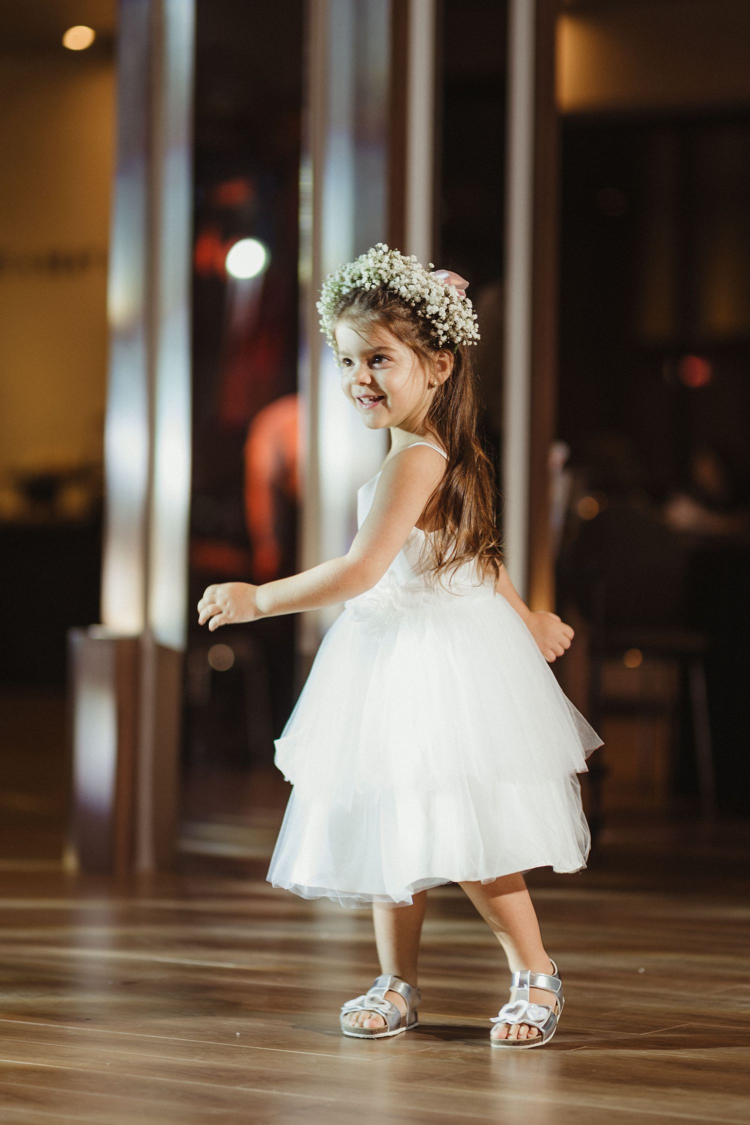 Adorable little girl in white tulle dress and flower crown dancing at a wedding reception.