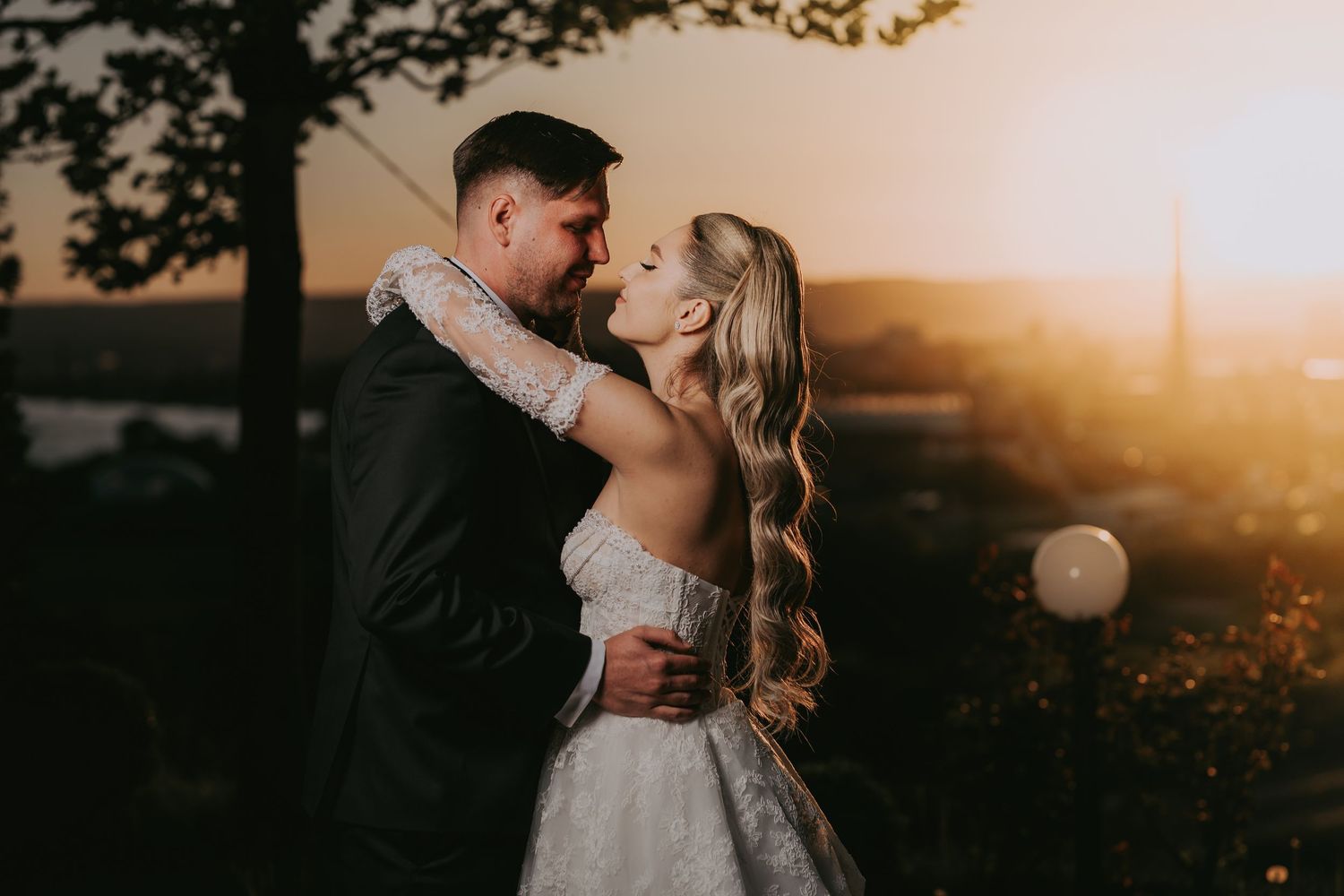 Romantic couple almost kissing at golden sunset with bride in lace gown and long blonde hair.