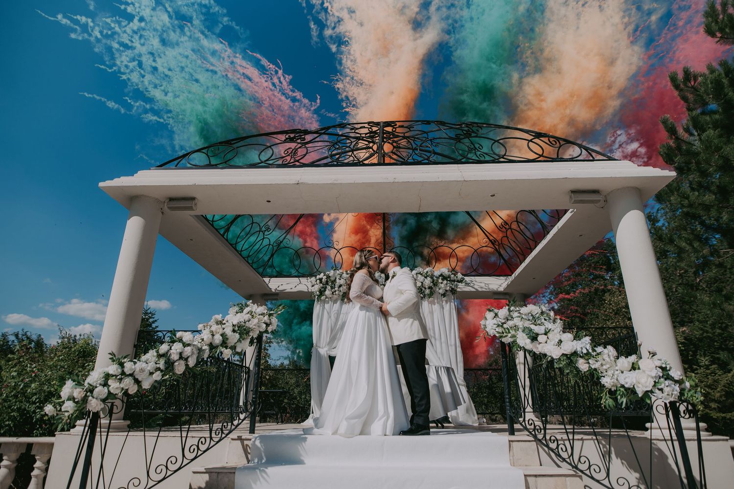 Couple exchanging vows under a white gazebo with colorful powder cannons exploding in the sky. Epicu Fotograf Drobeta-Turnu Severin