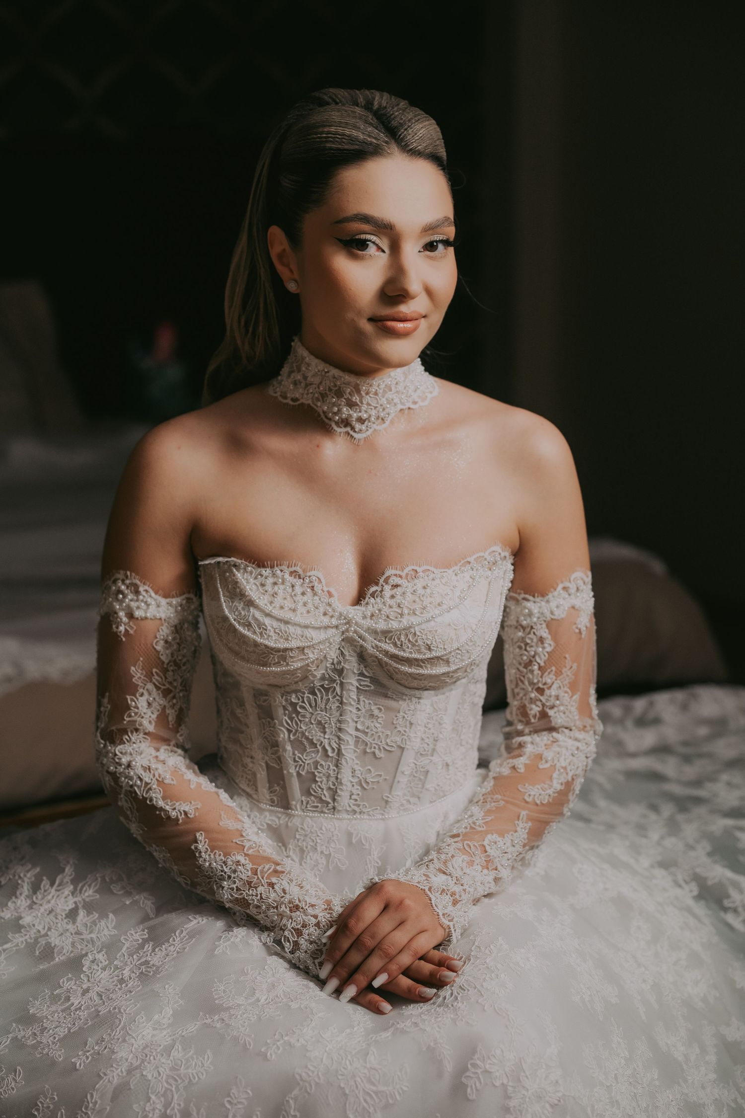 Beautiful bride in off-shoulder lace corset wedding gown sitting gracefully.