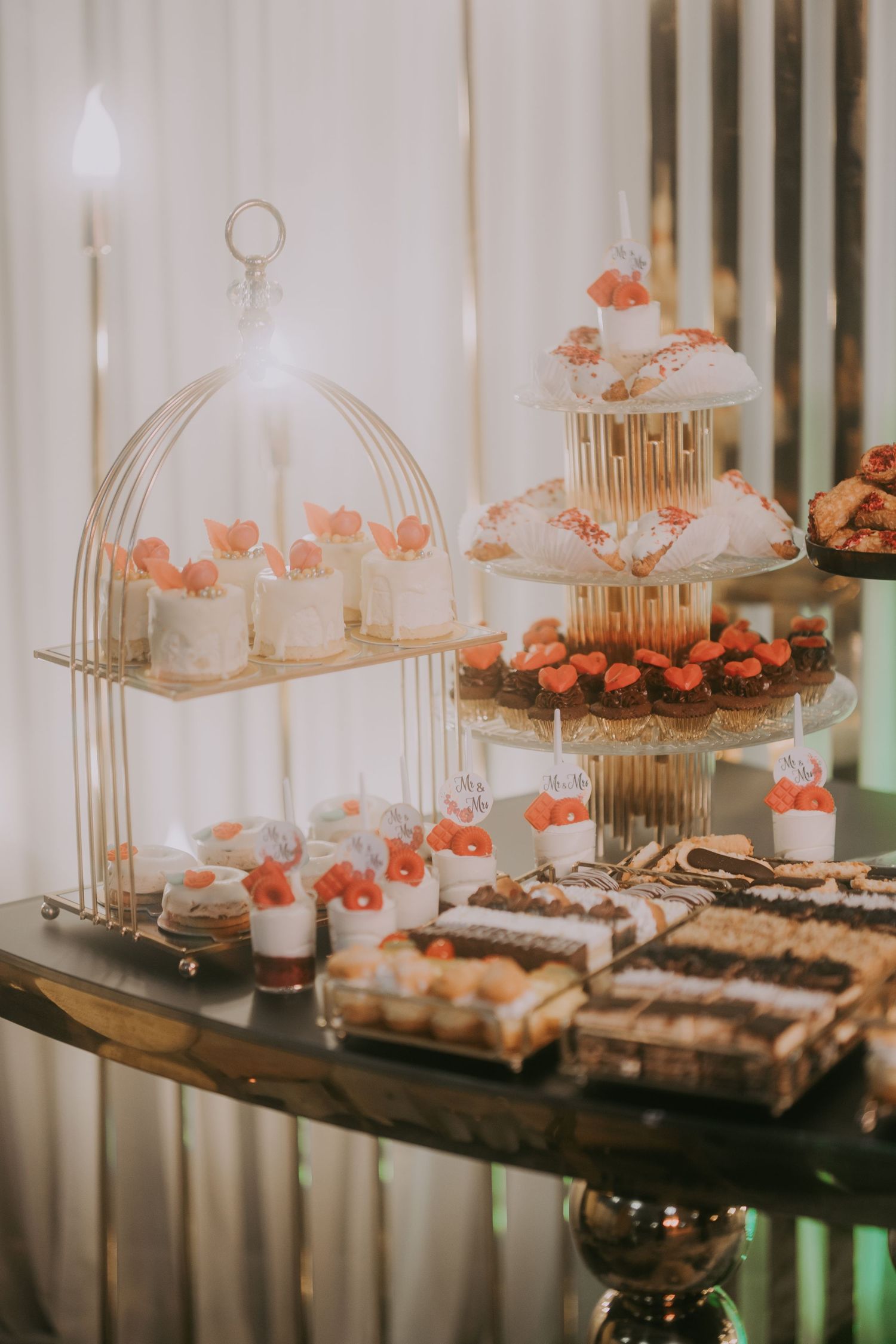 Elegant wedding dessert table with gold birdcage display, mini cakes, cupcakes, and petit fours. Epicu Fotograf Drobeta-Turnu Severin