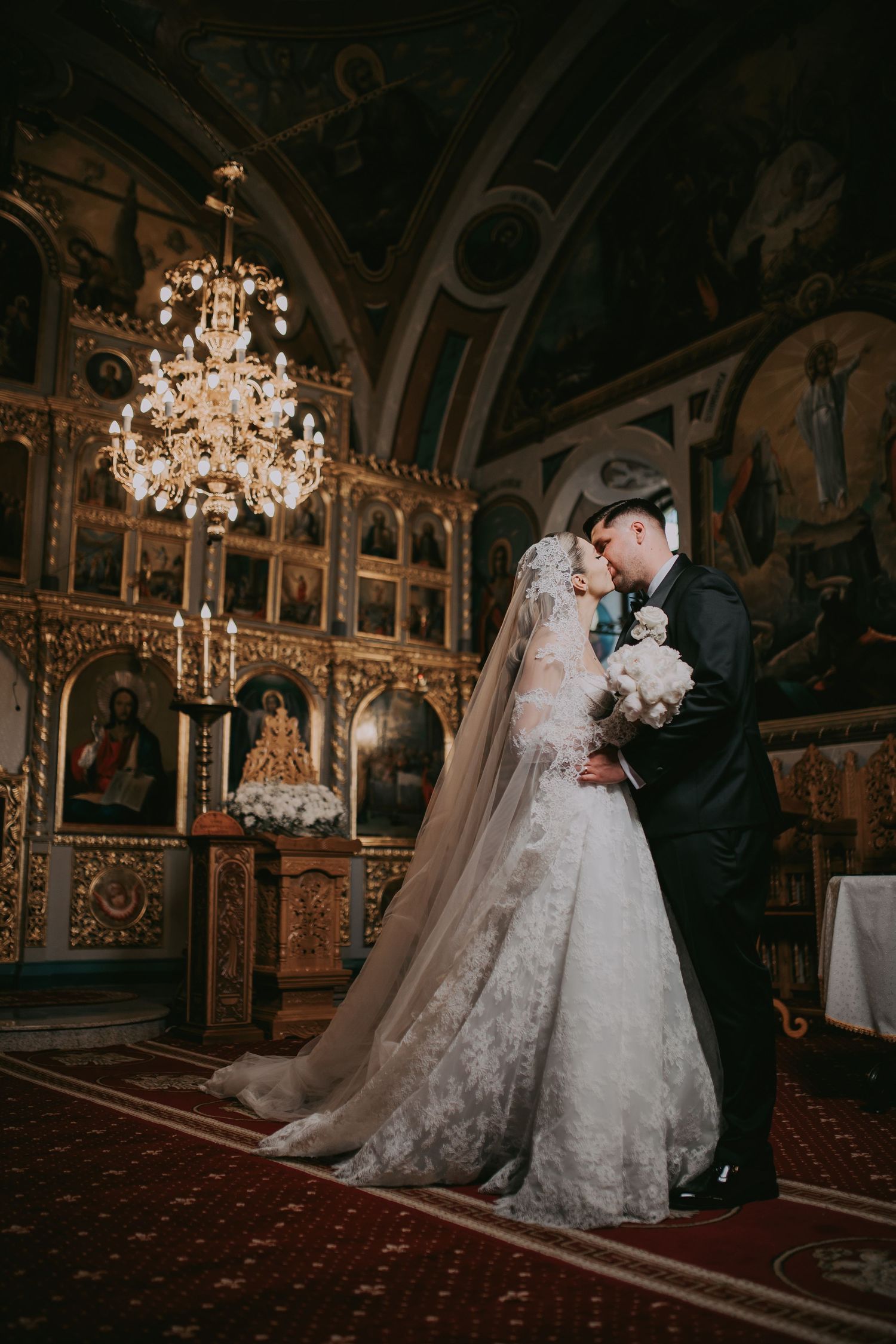 Bride and groom sharing intimate moment inside ornate Orthodox church.