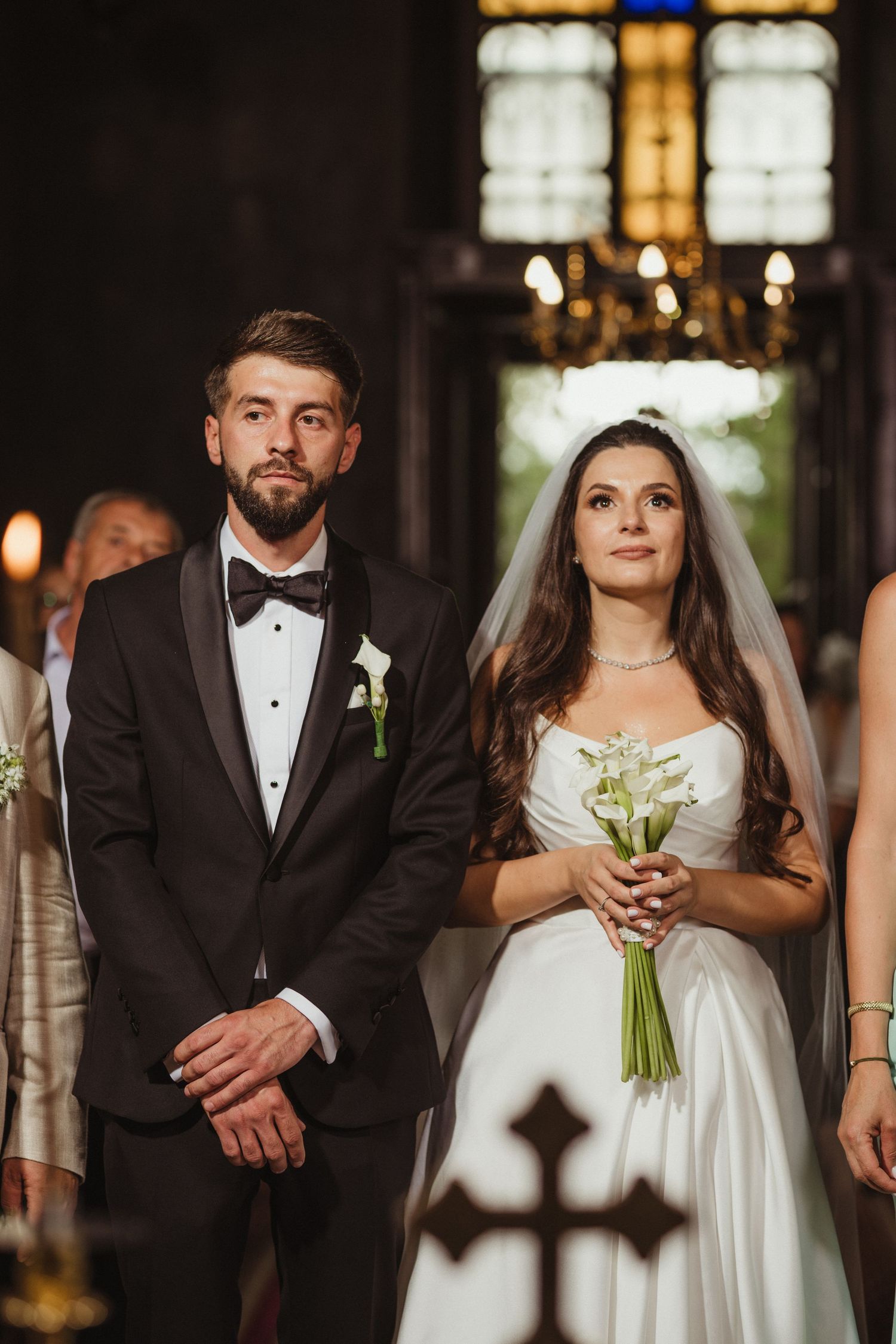 Bride and groom standing solemnly during their traditional church wedding ceremony holding a white bouquet.