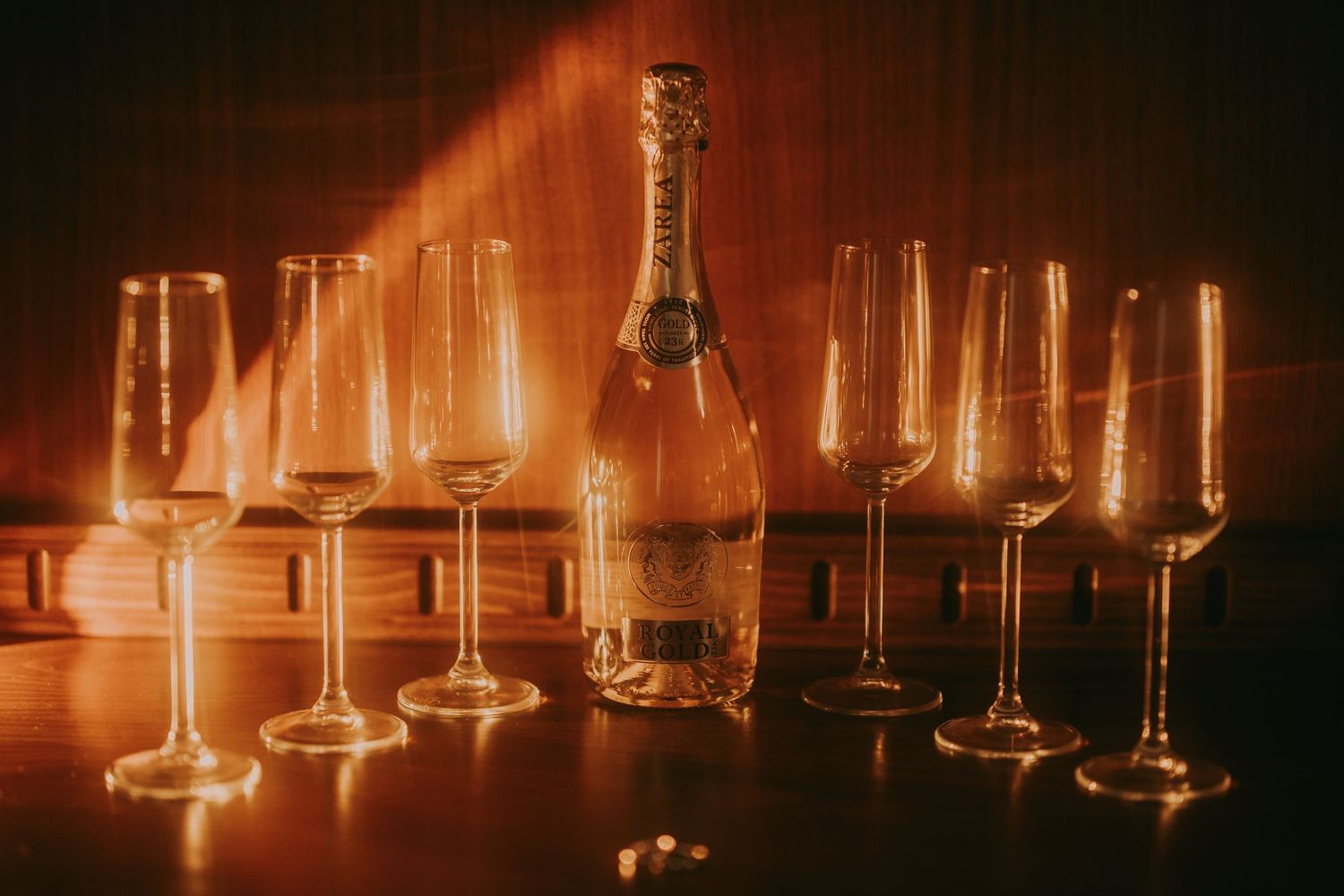 Champagne bottle surrounded by elegant crystal flutes glowing in warm golden light on a wooden table. Epicu Fotograf Drobeta-Turnu Severin