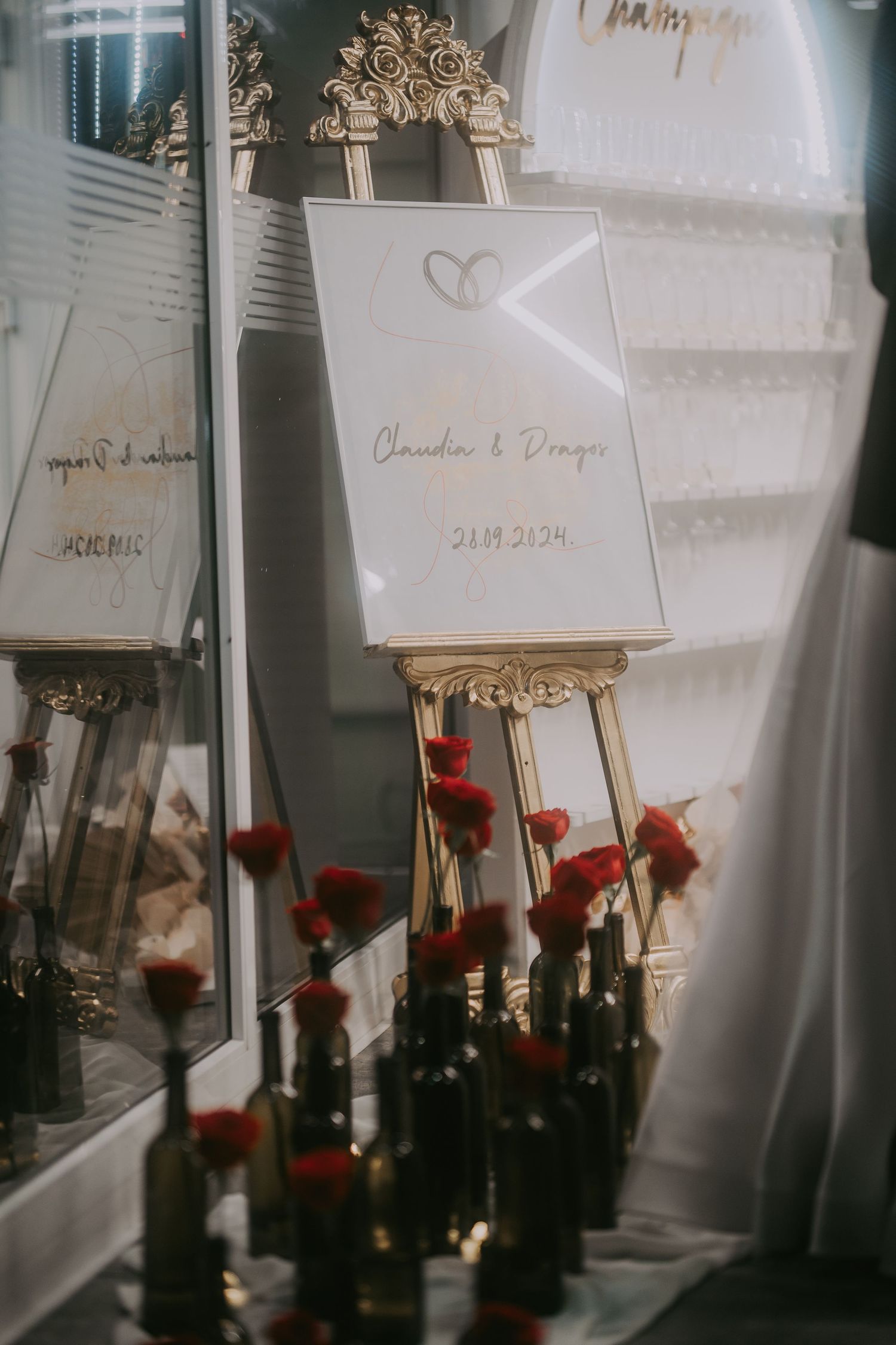 Elegant wedding welcome sign on gold easel with red roses in dark wine bottles at Hill Events venue. Epicu Fotograf Drobeta-Turnu Severin