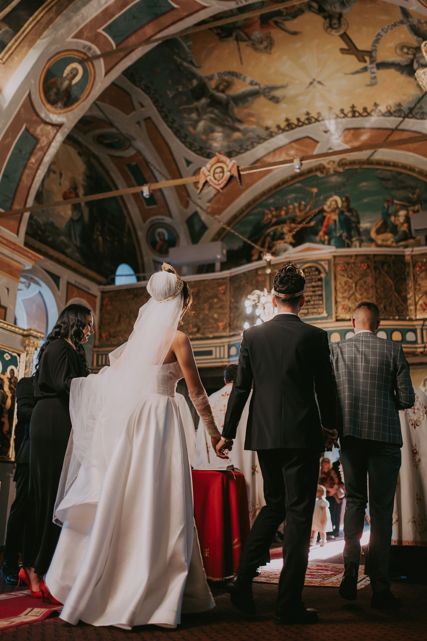 Bride and groom holding hands at altar of ornate Orthodox church with painted frescoes. Epicu Fotograf Drobeta-Turnu Severin