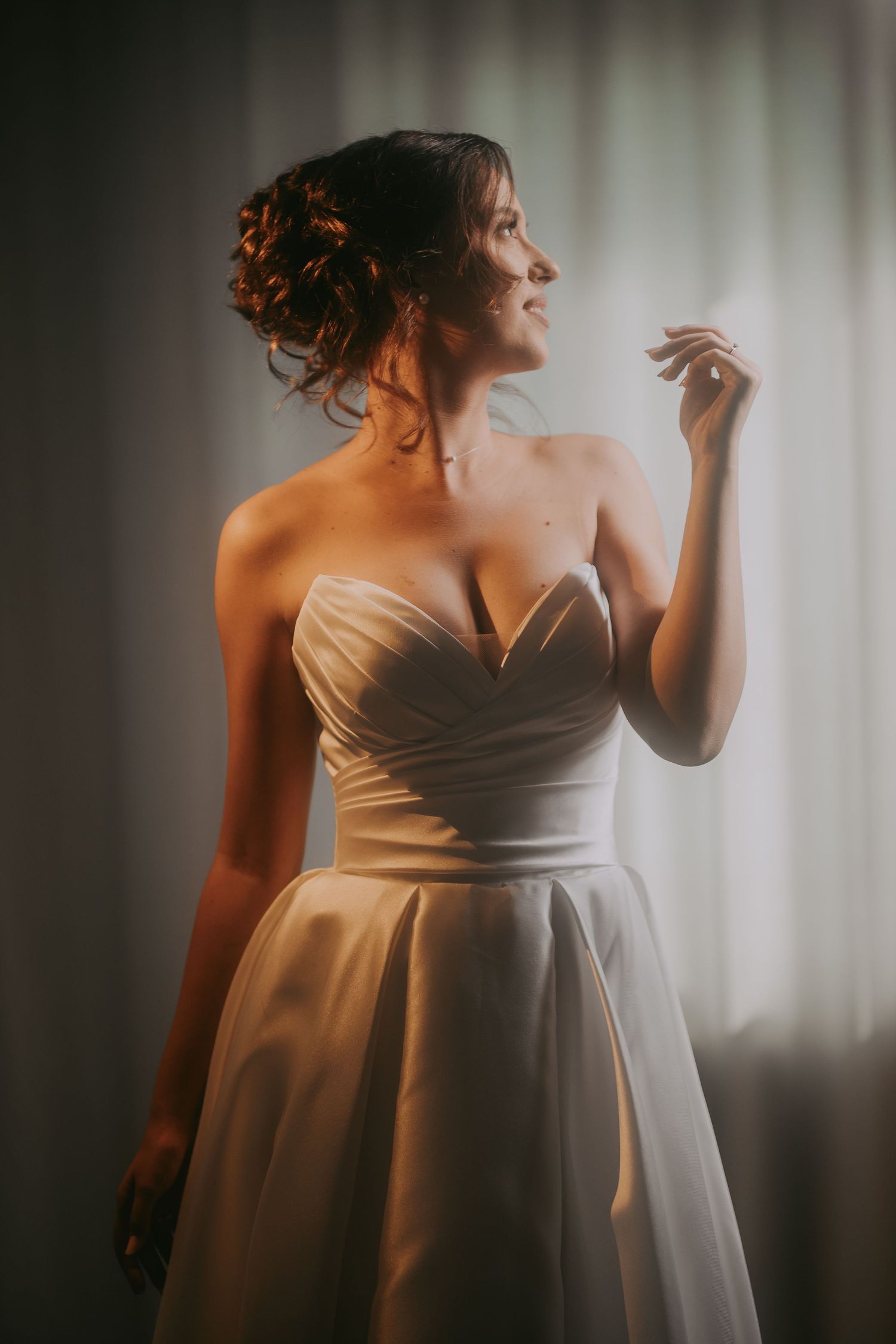 Radiant bride in a strapless satin wedding gown posing gracefully by a softly lit window. Epicu Fotograf Drobeta-Turnu Severin