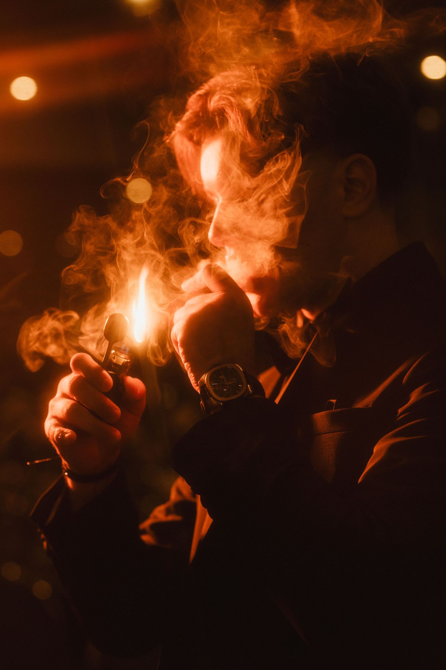 Man lighting a cigarette with a lighter surrounded by dramatic smoke in warm amber light at night.