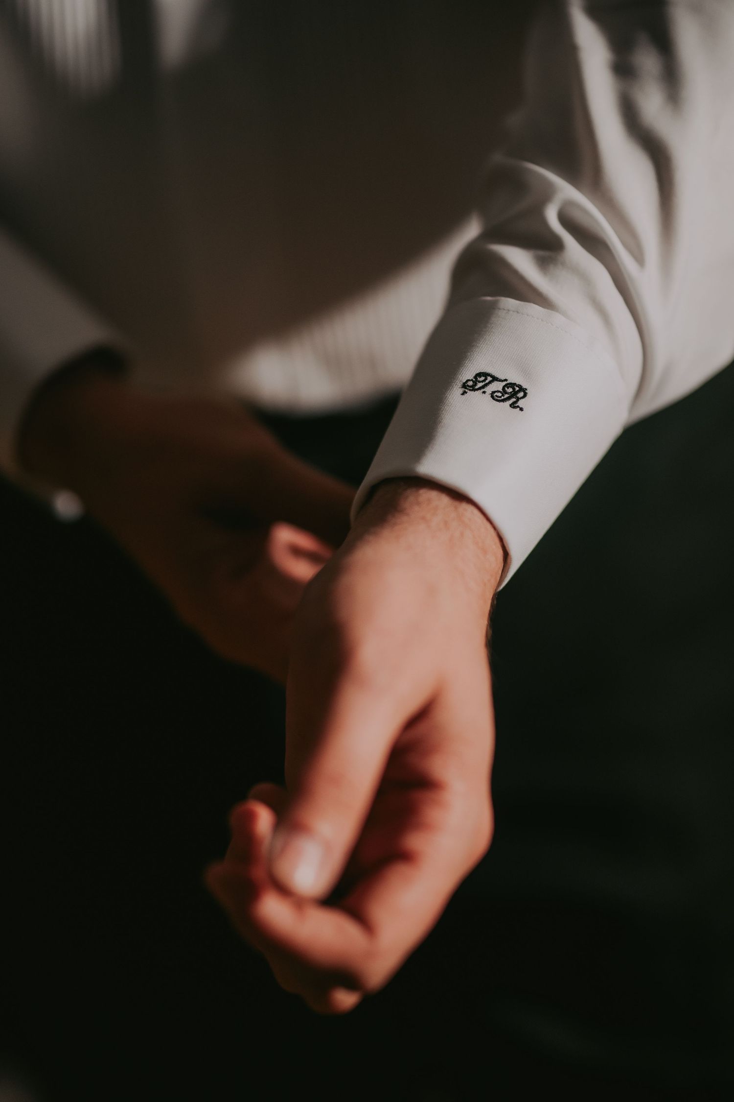 Groom adjusting monogrammed white dress shirt cuff before wedding ceremony.