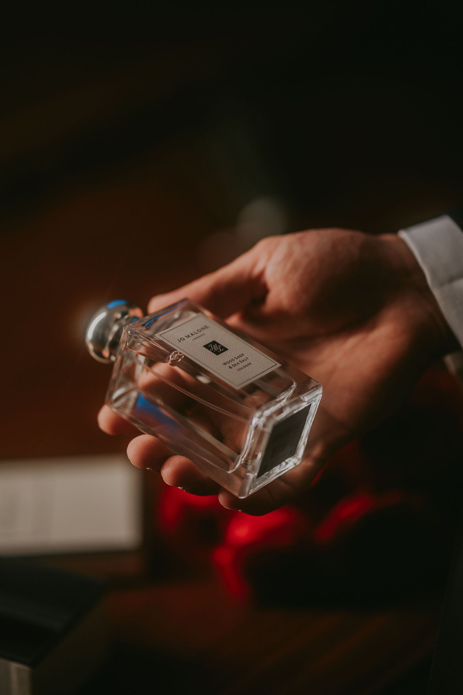Groom holding a Jo Malone perfume bottle with red roses in the background. Epicu Fotograf Drobeta-Turnu Severin