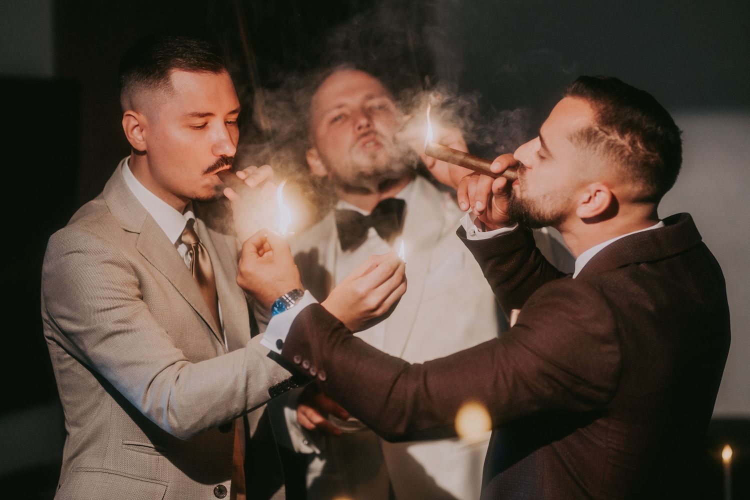 Three groomsmen lighting cigars together in a dramatic nighttime wedding celebration moment. Epicu Fotograf Drobeta-Turnu Severin