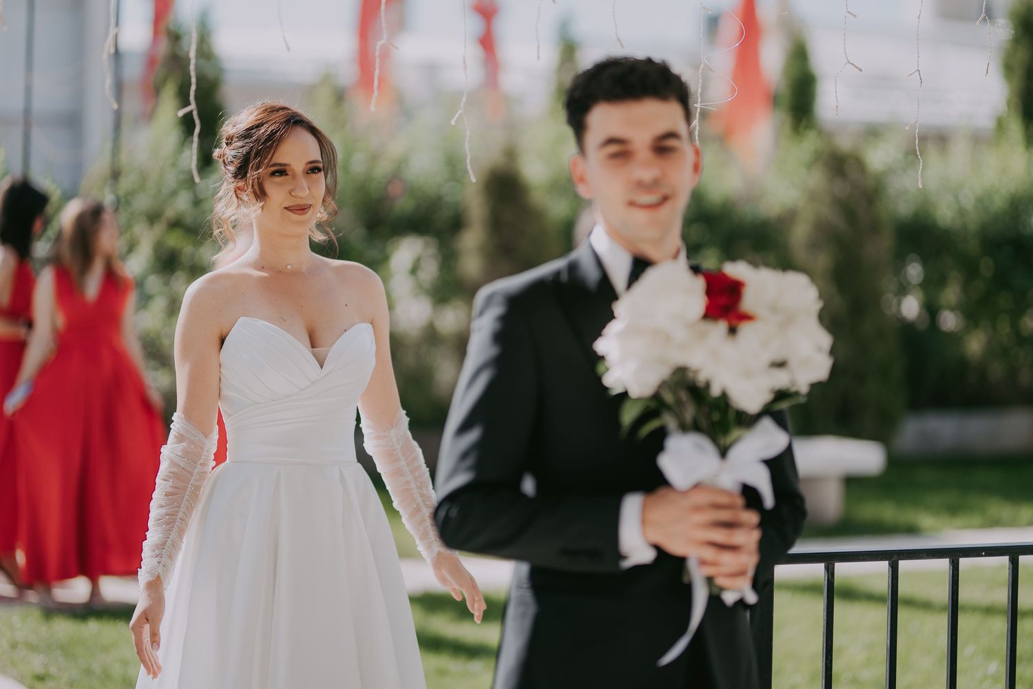 Bride in white lace wedding gown standing before groom holding a red and white bouquet. Epicu Fotograf Drobeta-Turnu Severin