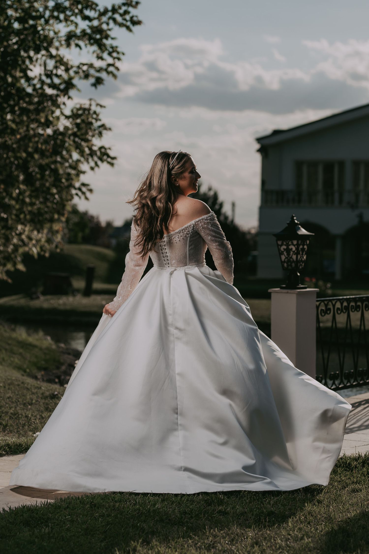 Bride in elegant off-shoulder lace wedding gown with full skirt poses in garden setting. Epicu Fotograf Drobeta-Turnu Severin