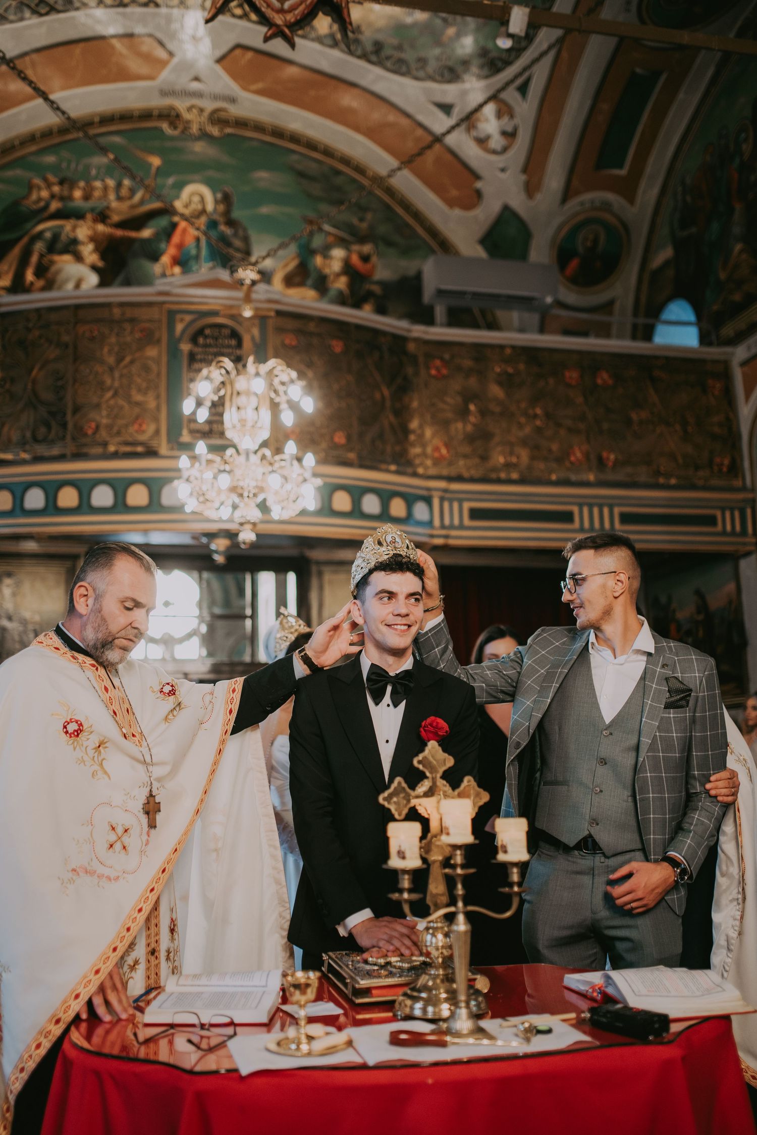 Orthodox priest crowning groom during traditional wedding ceremony at red-draped altar. Epicu Fotograf Drobeta-Turnu Severin