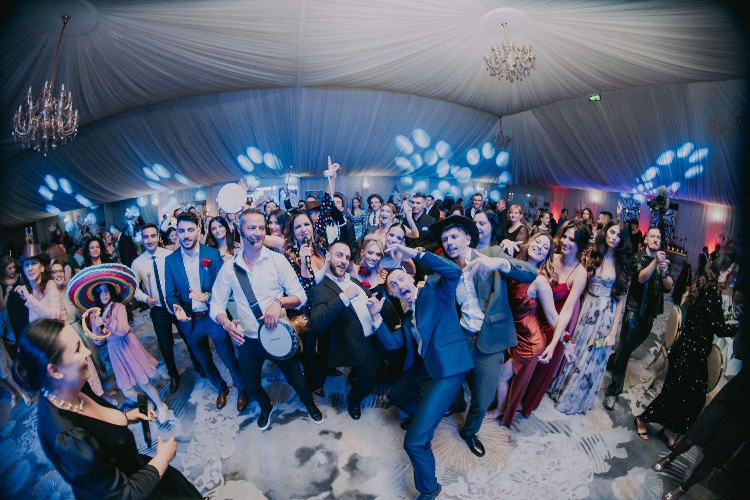 Large wedding reception crowd celebrating on the dance floor under blue lights in elegant tent venue. Epicu Fotograf Drobeta-Turnu Severin
