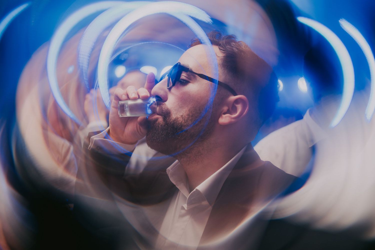 Man in glasses drinking a shot glass captured with swirling blue light painting effect at a wedding reception. Epicu Fotograf Drobeta-Turnu