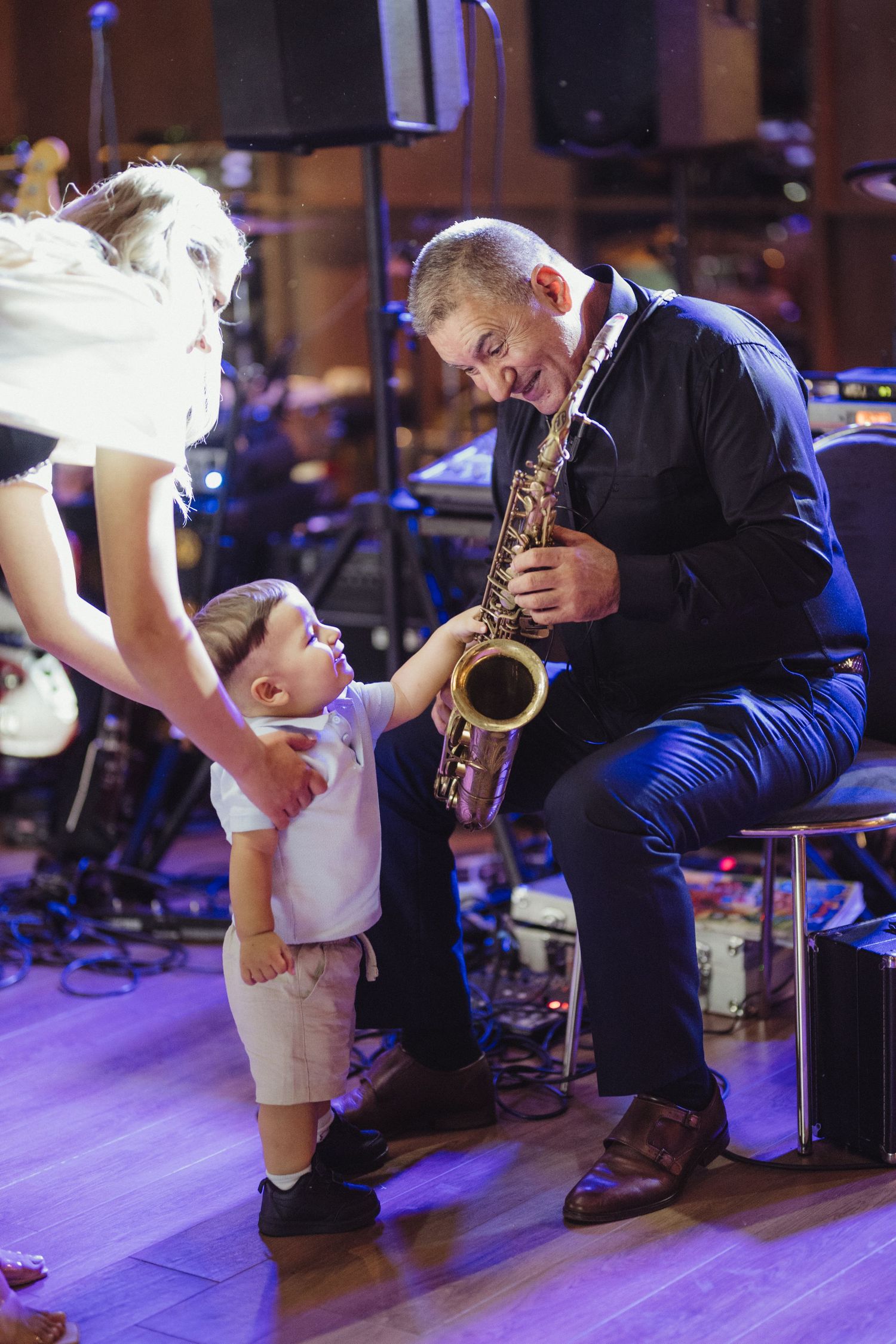 Curious toddler reaches toward saxophone as musician performs at colorful wedding reception. Epicu Fotograf Drobeta-Turnu Severin