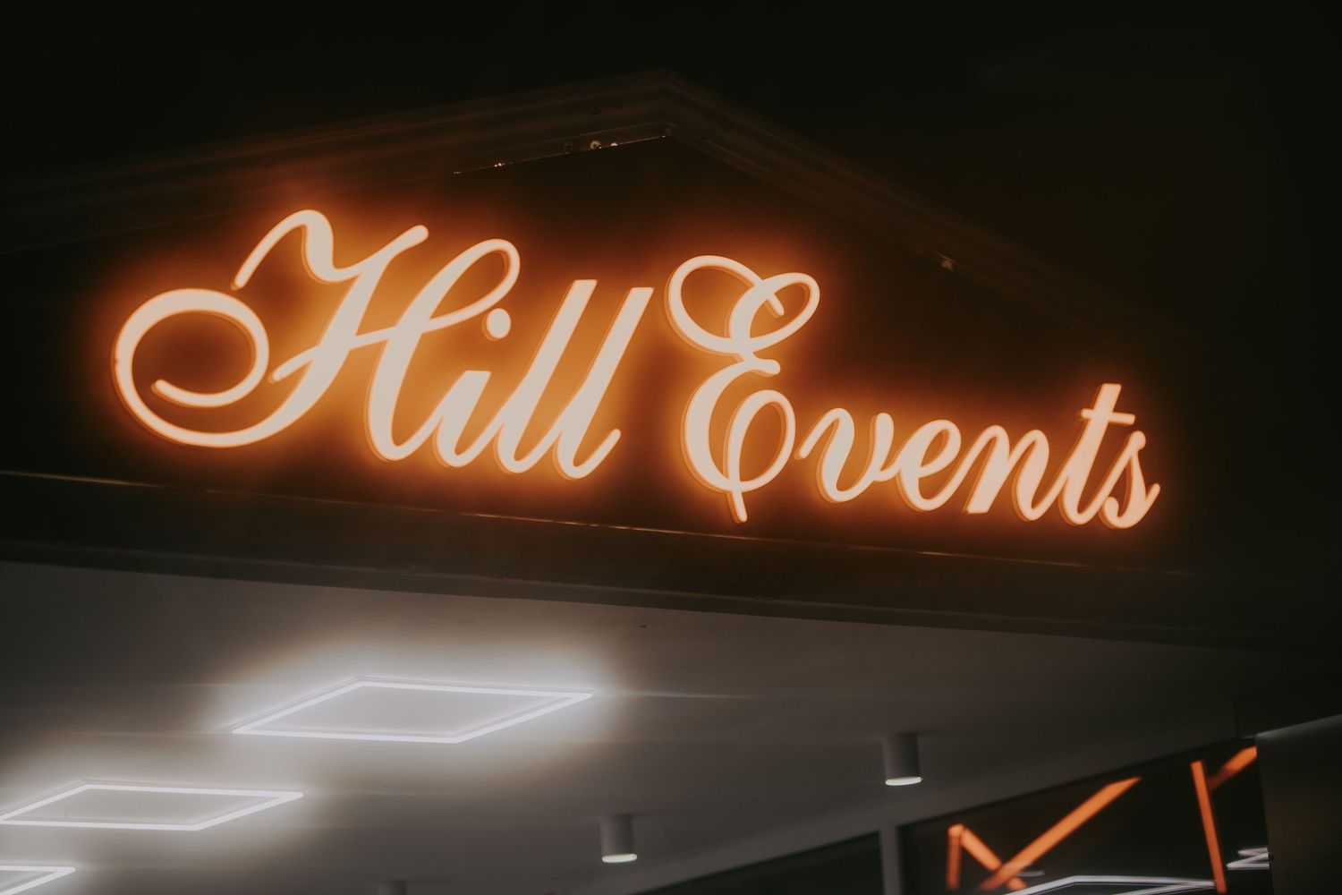 Glowing orange neon sign reading Hill Events mounted on dark ceiling of event venue. Epicu Fotograf Drobeta-Turnu Severin