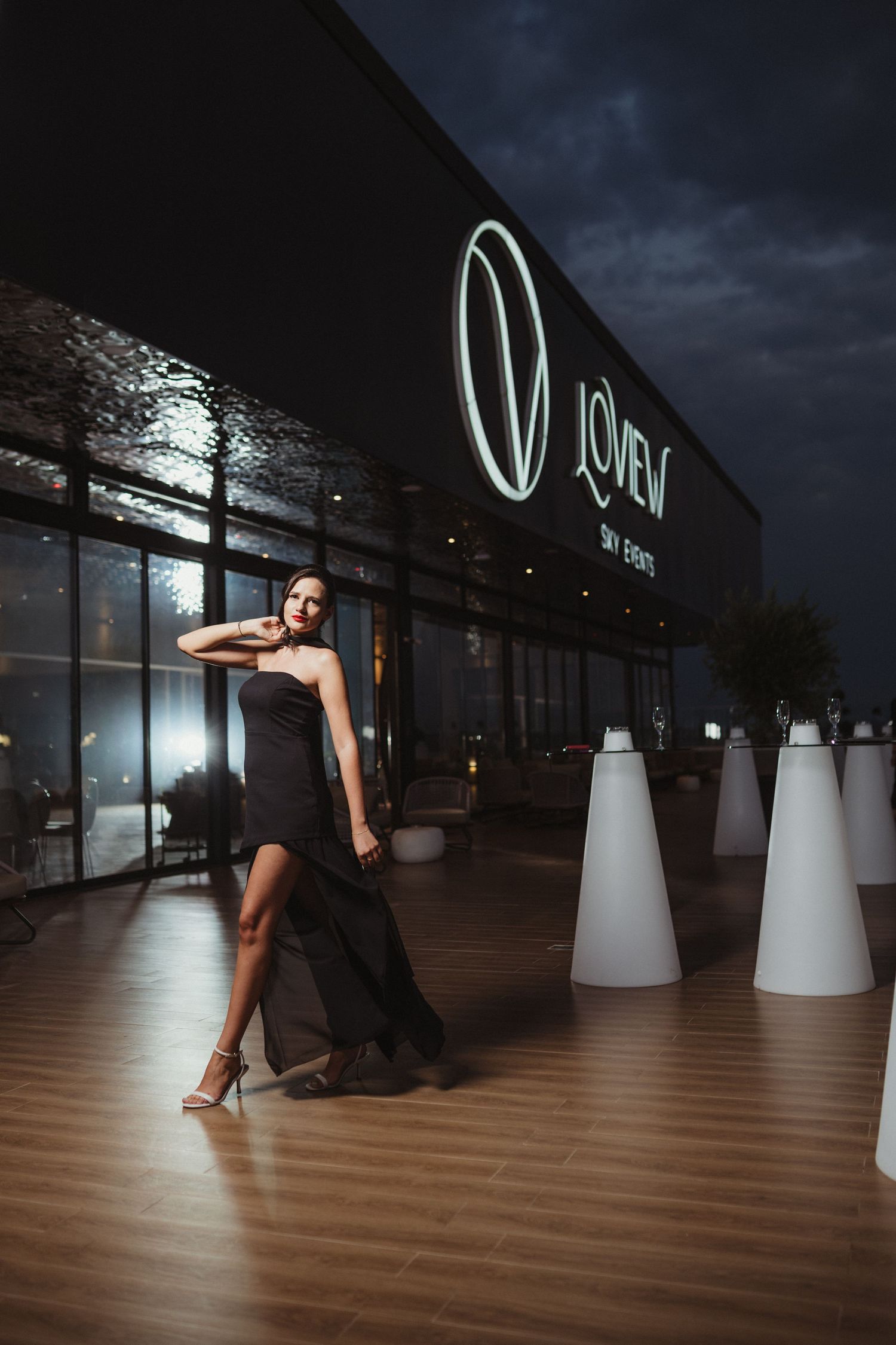 Elegant woman in black strapless gown poses outside LoveView Sky Events venue at night.