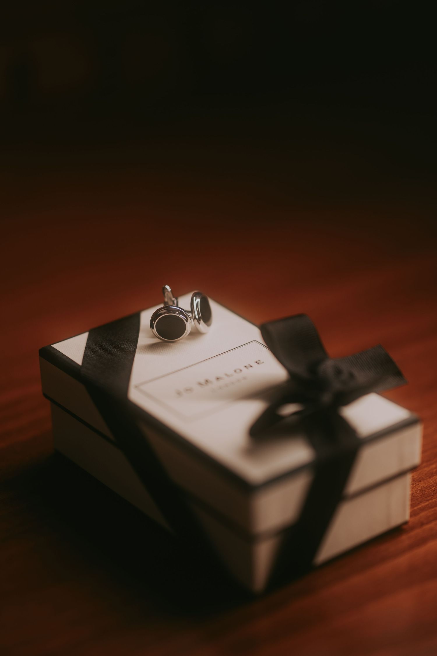 Elegant silver cufflinks resting on a Jo Malone gift box tied with black ribbon on wooden surface. Epicu Fotograf Drobeta-Turnu Severin