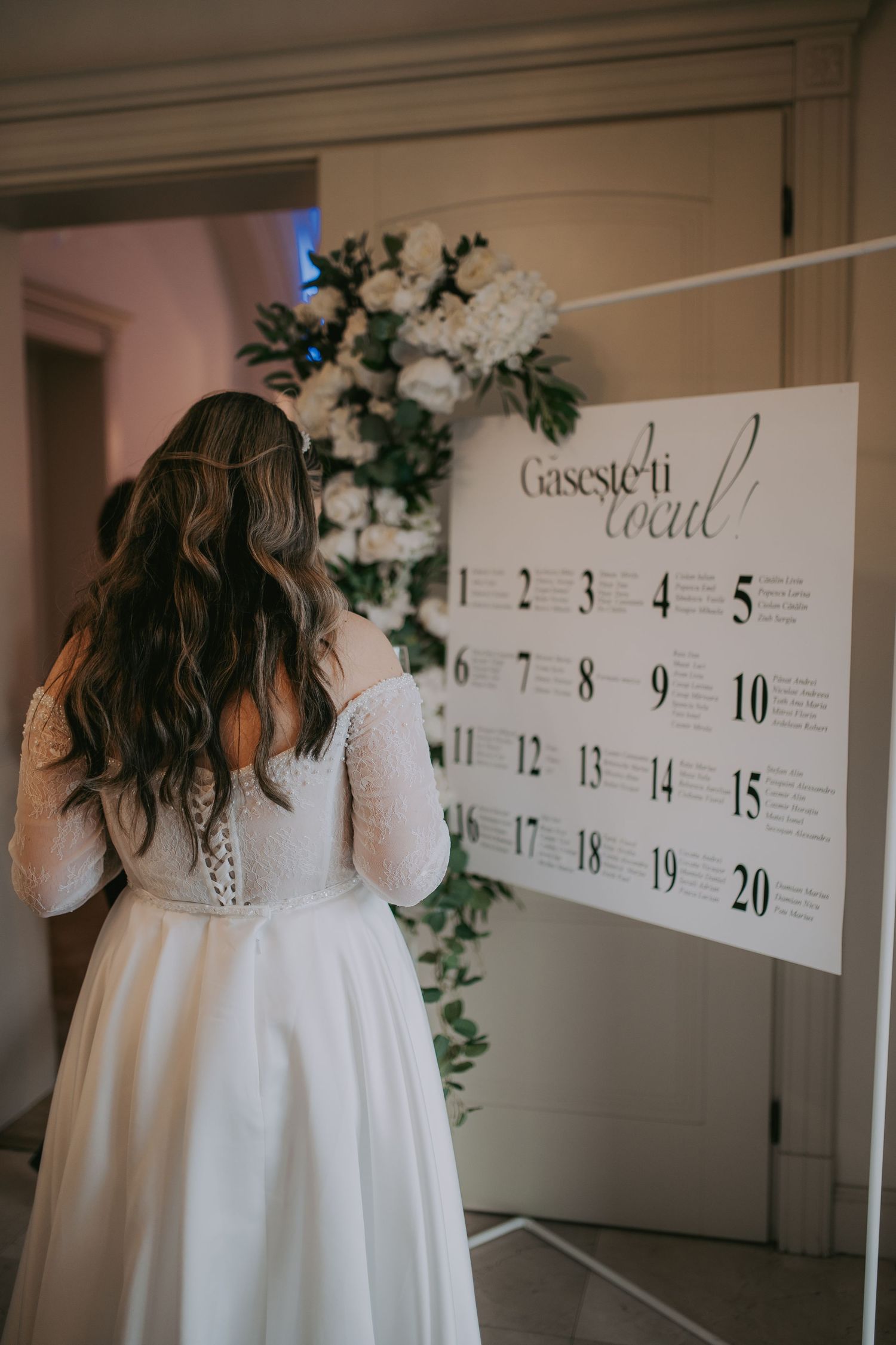 Bride in lace wedding gown reviews seating chart display decorated with white floral arrangements. Epicu Fotograf Drobeta-Turnu Severin