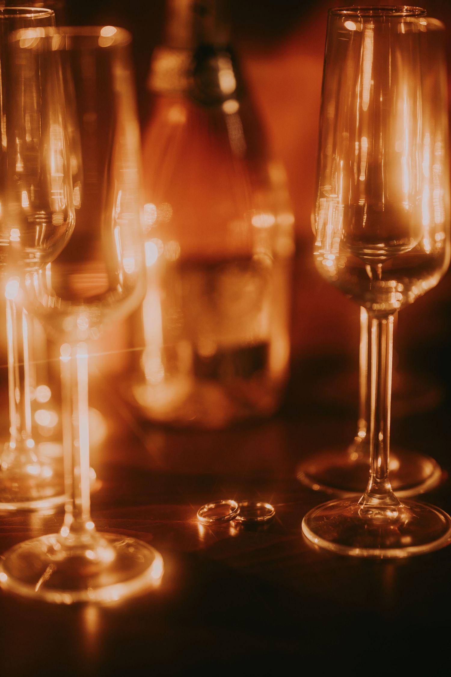 Wedding rings placed between crystal champagne flutes with warm bokeh lighting in the background. Epicu Fotograf Drobeta-Turnu Severin