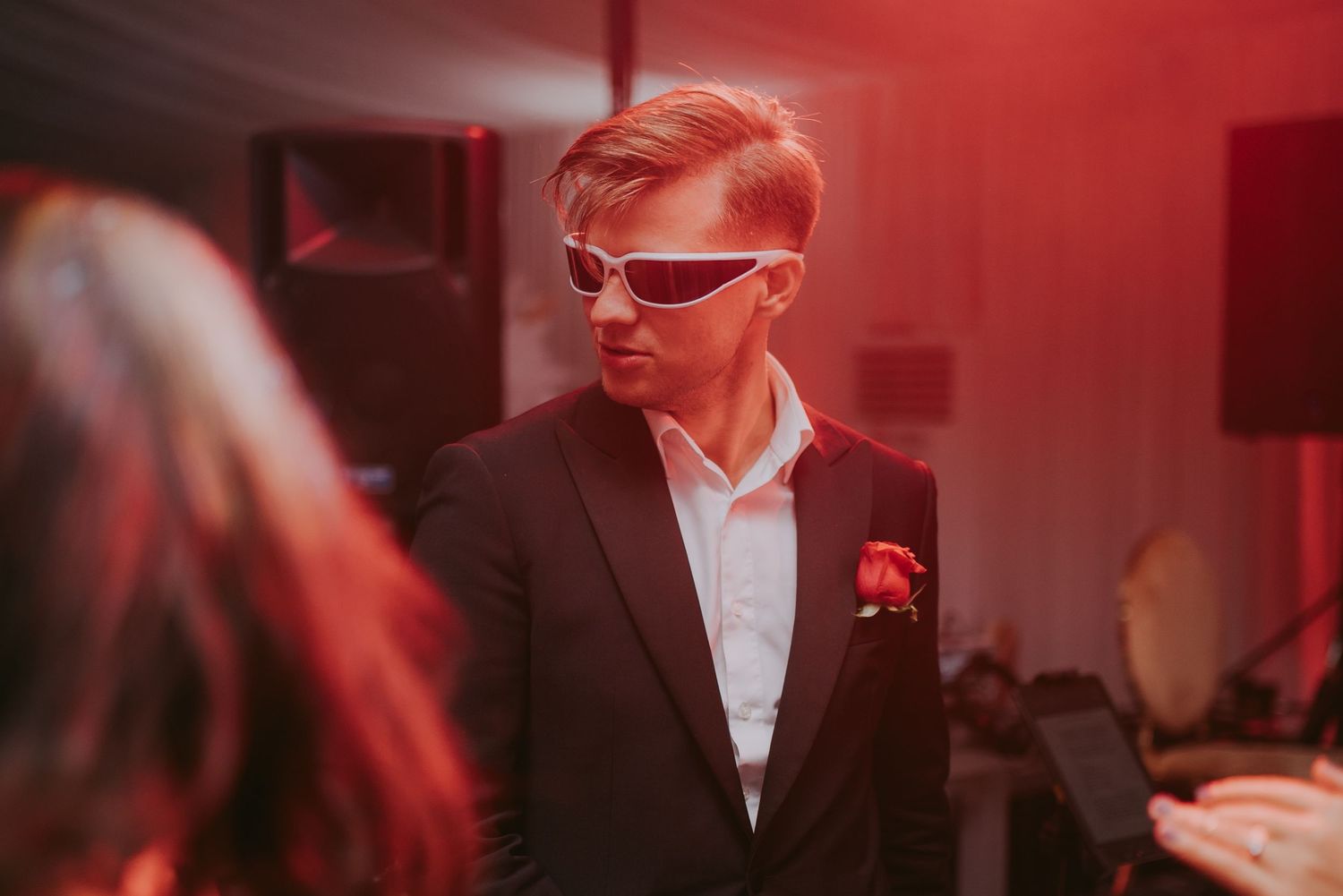 Stylish man in black suit wearing futuristic sunglasses at a red-lit wedding reception. Epicu Fotograf Drobeta-Turnu Severin