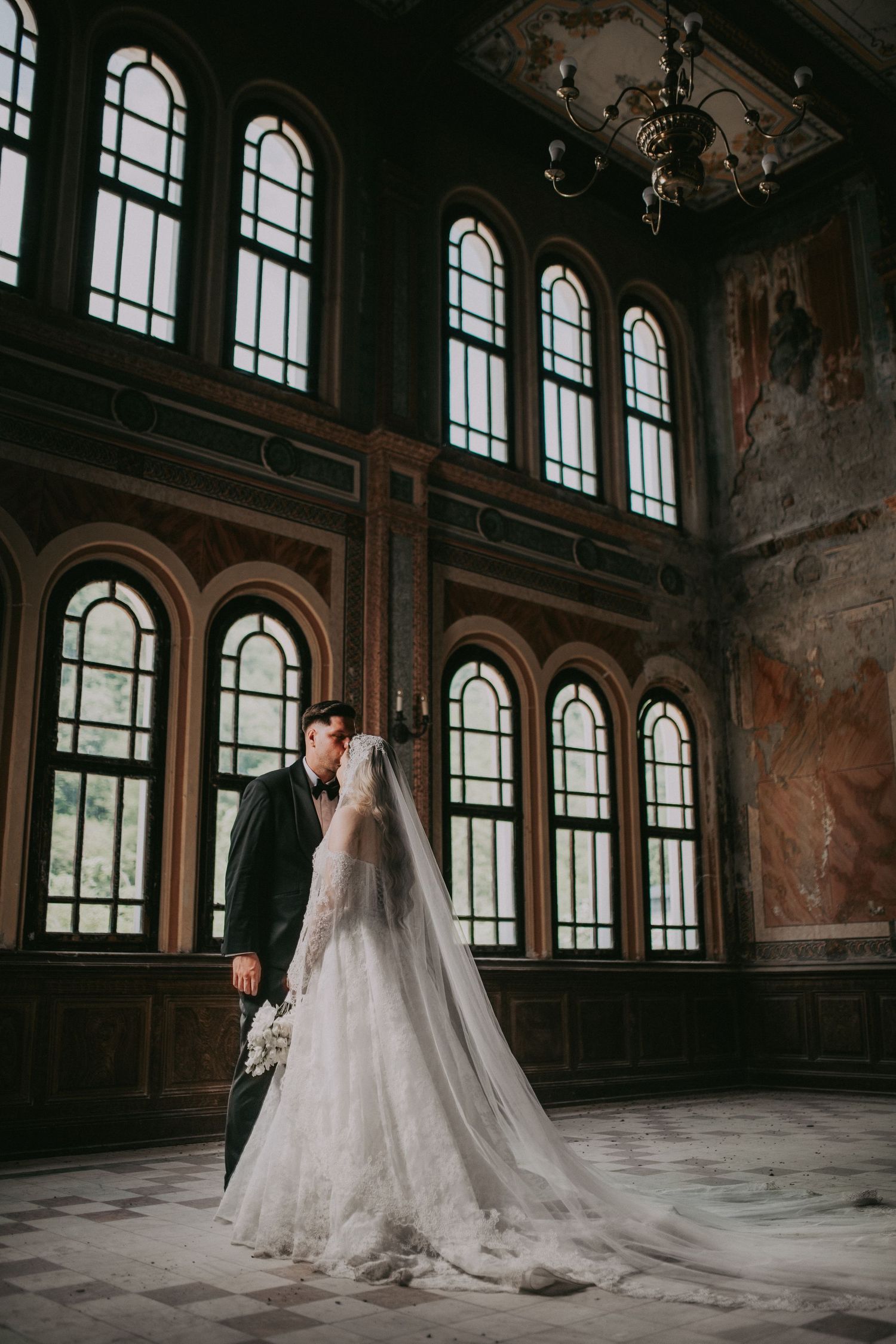 Bride and groom sharing an intimate moment in a grand historic hall with arched windows and murals.Epicu Fotograf Drobeta-Turnu Severin