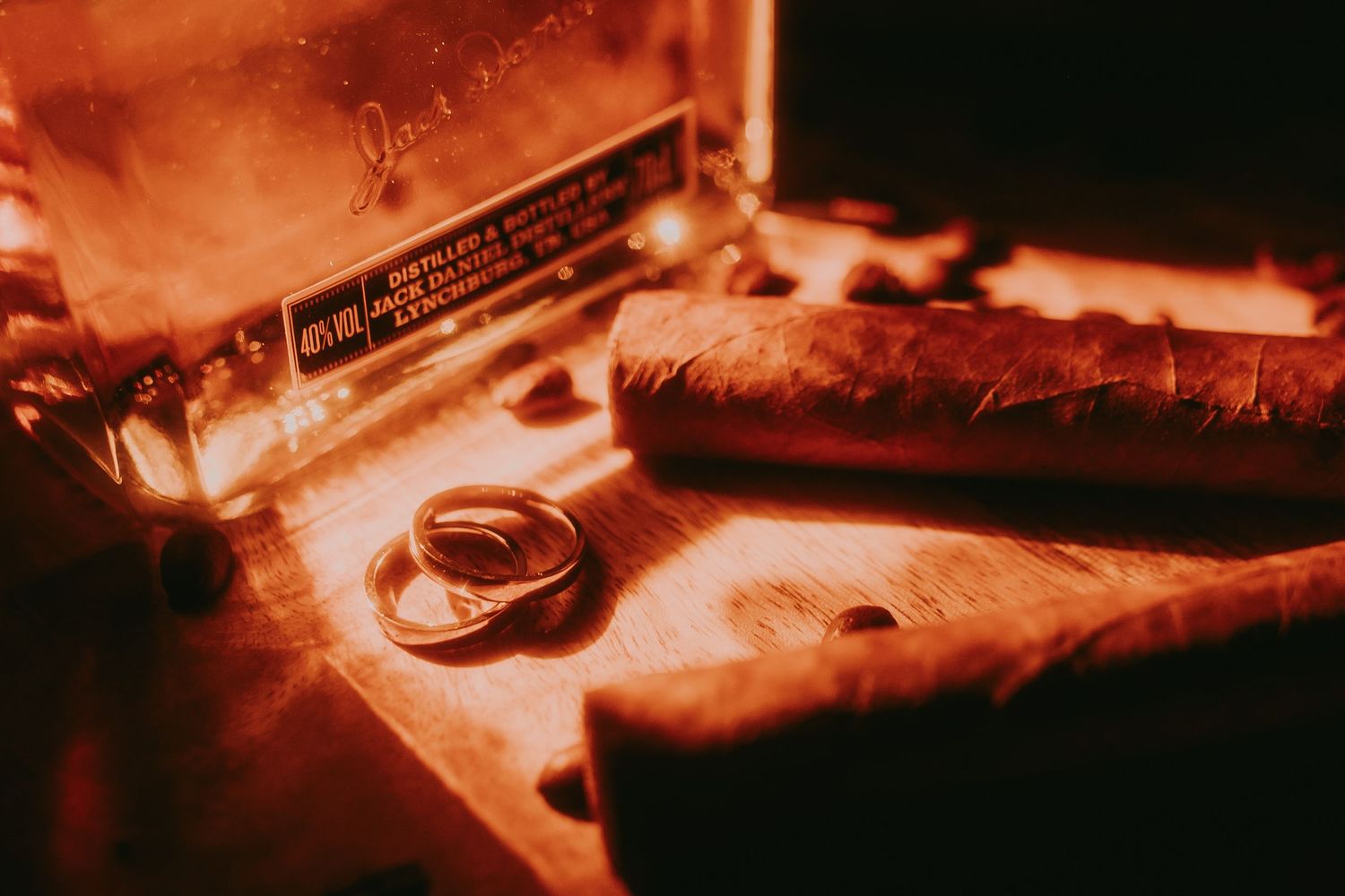 Gold wedding rings resting beside cigars in a wooden cigar box in warm amber light.