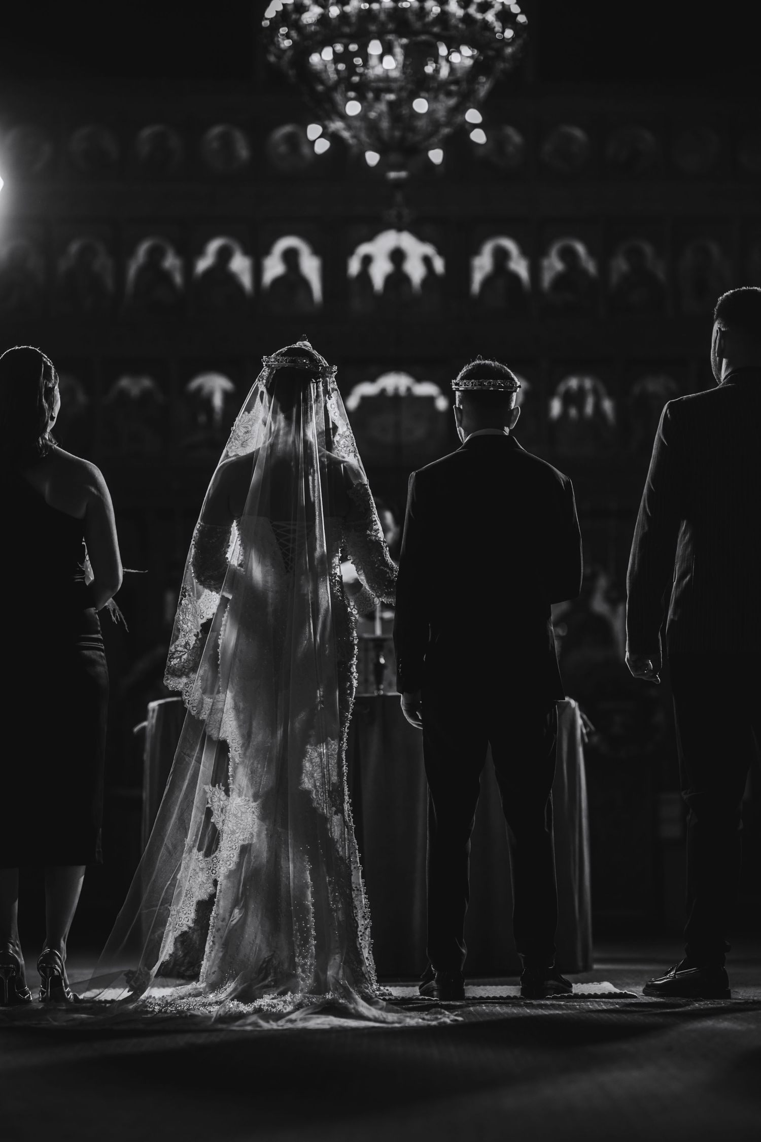 Black and white photo of bride in lace veil standing at church altar during wedding ceremony.