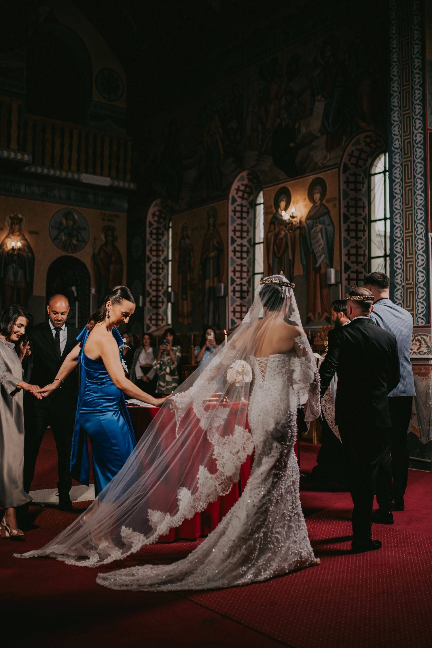 Bride in lace cathedral veil and fitted gown at Orthodox church altar with religious icons in background.