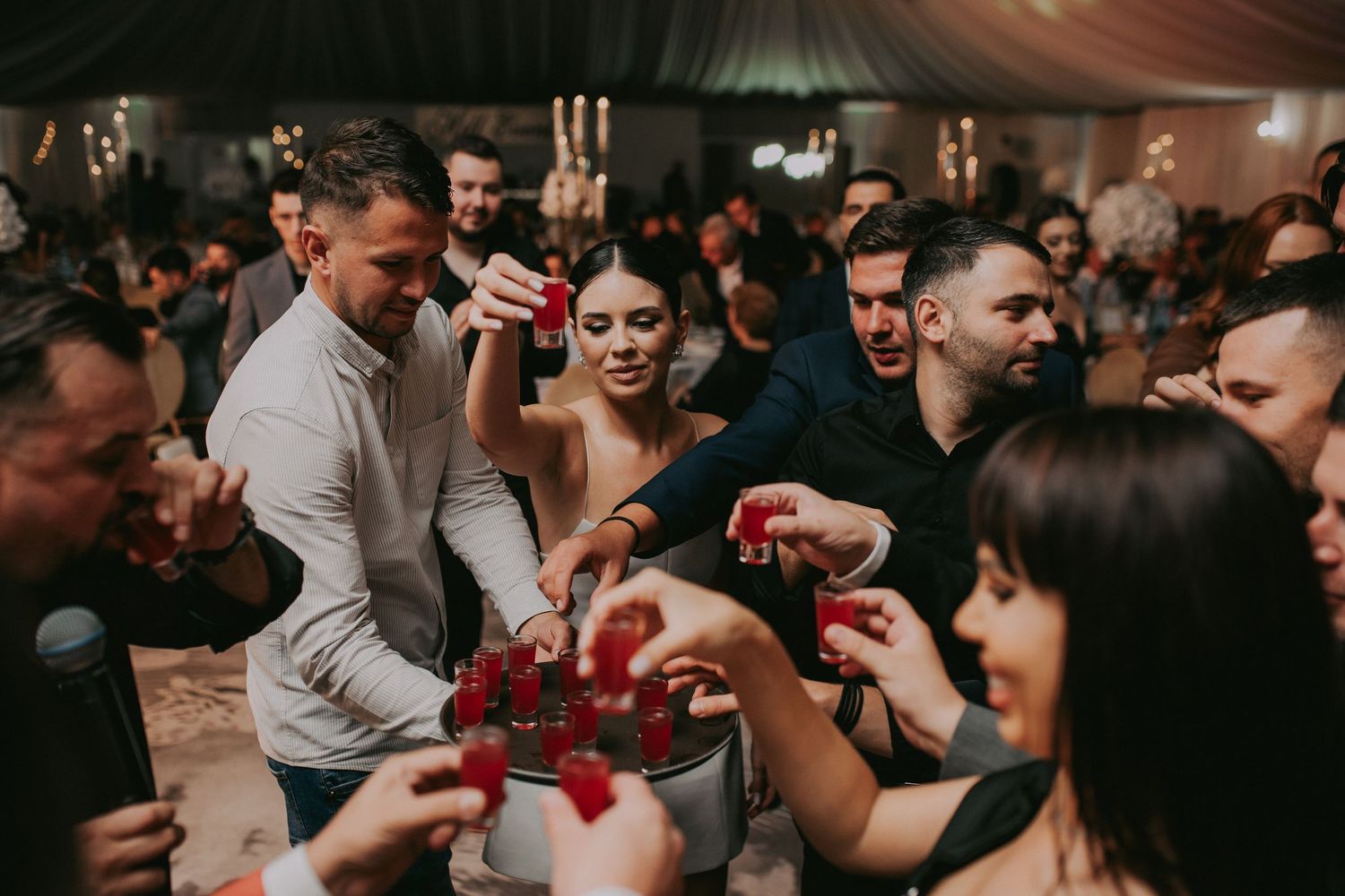 Wedding guests celebrating with red shot glasses at a lively indoor reception party.