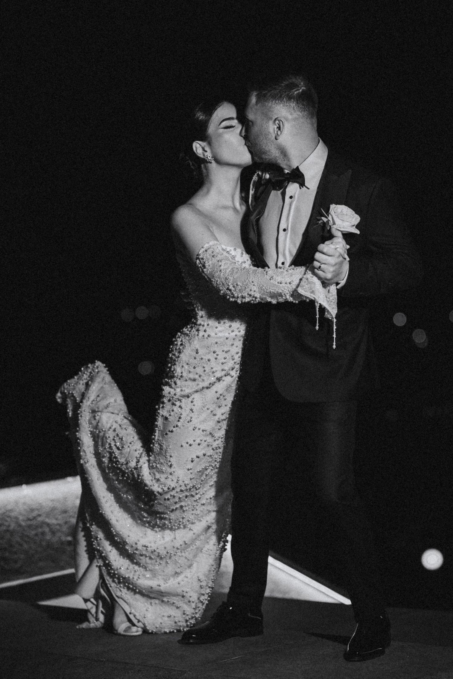 Black and white romantic photo of bride and groom sharing a passionate kiss outdoors at night.