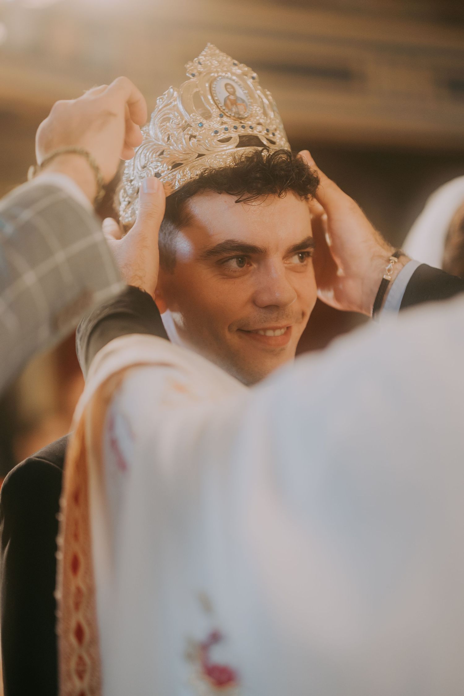 Groom smiles as ornate Orthodox wedding crown is placed on his head during church ceremony. Epicu Fotograf Drobeta-Turnu Severin