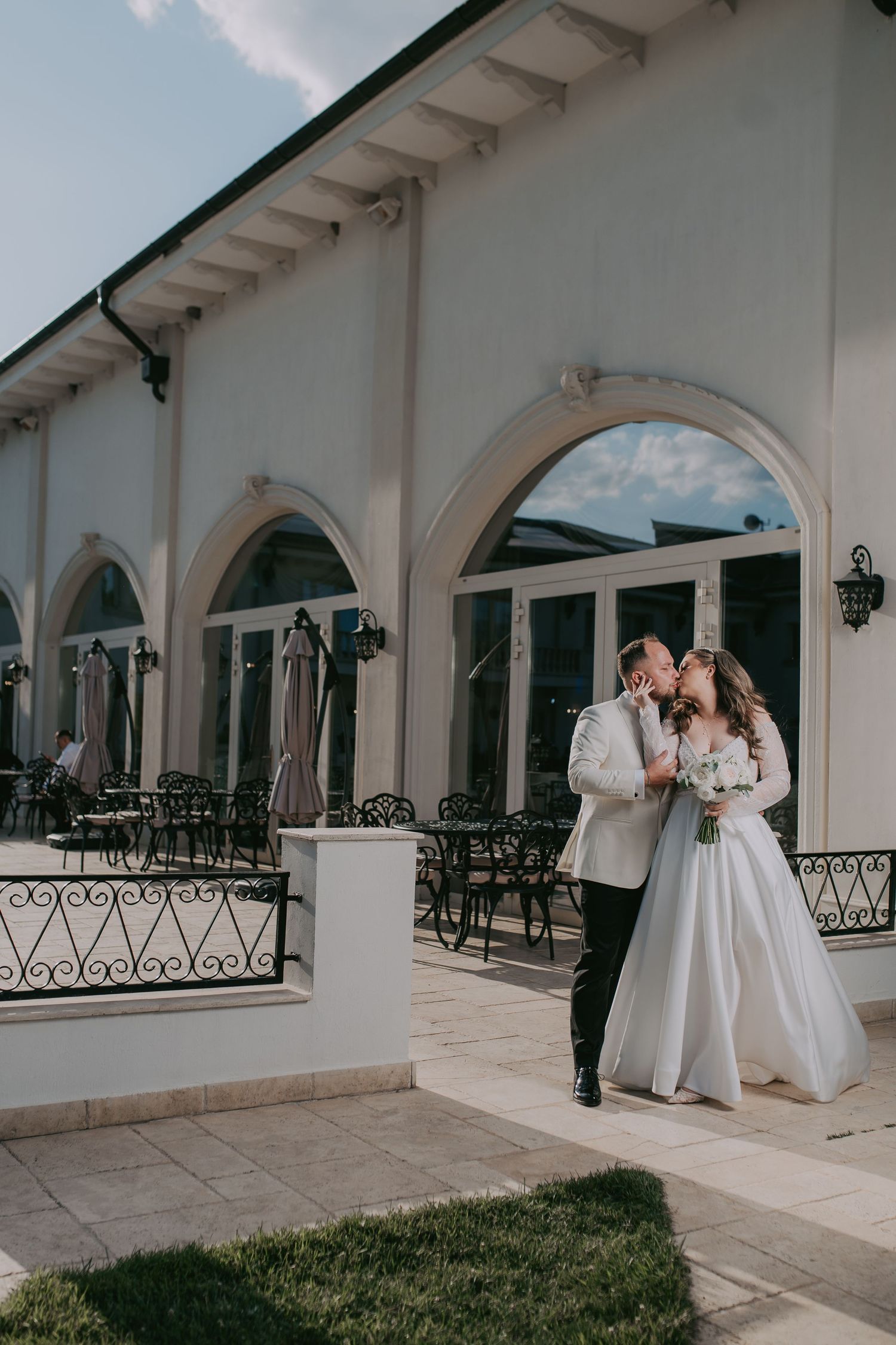 Bride and groom share a romantic kiss outside a white arched venue on their wedding day. Epicu Fotograf Drobeta-Turnu Severin
