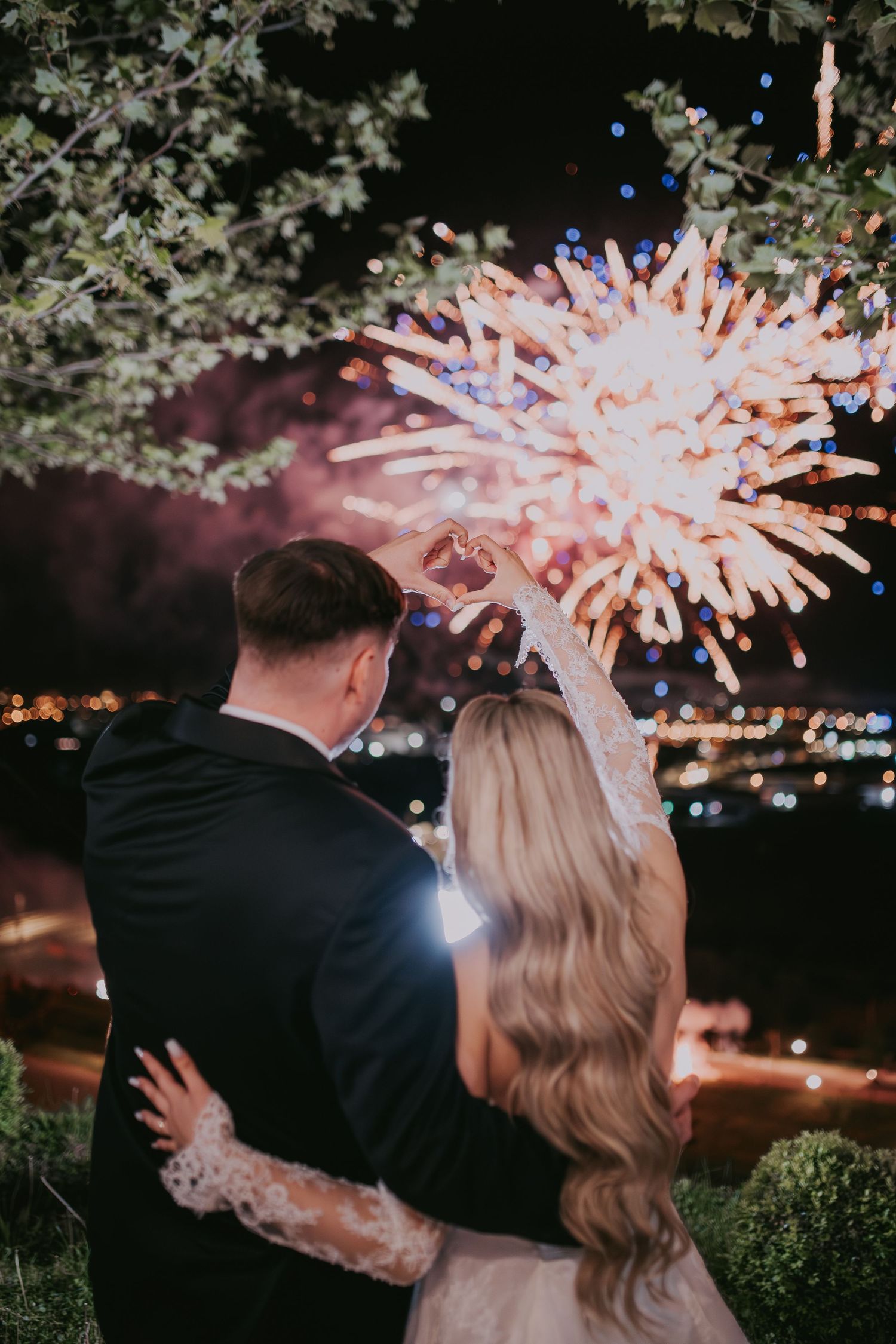 Newlywed couple embracing while watching colorful fireworks display light up the night sky together.