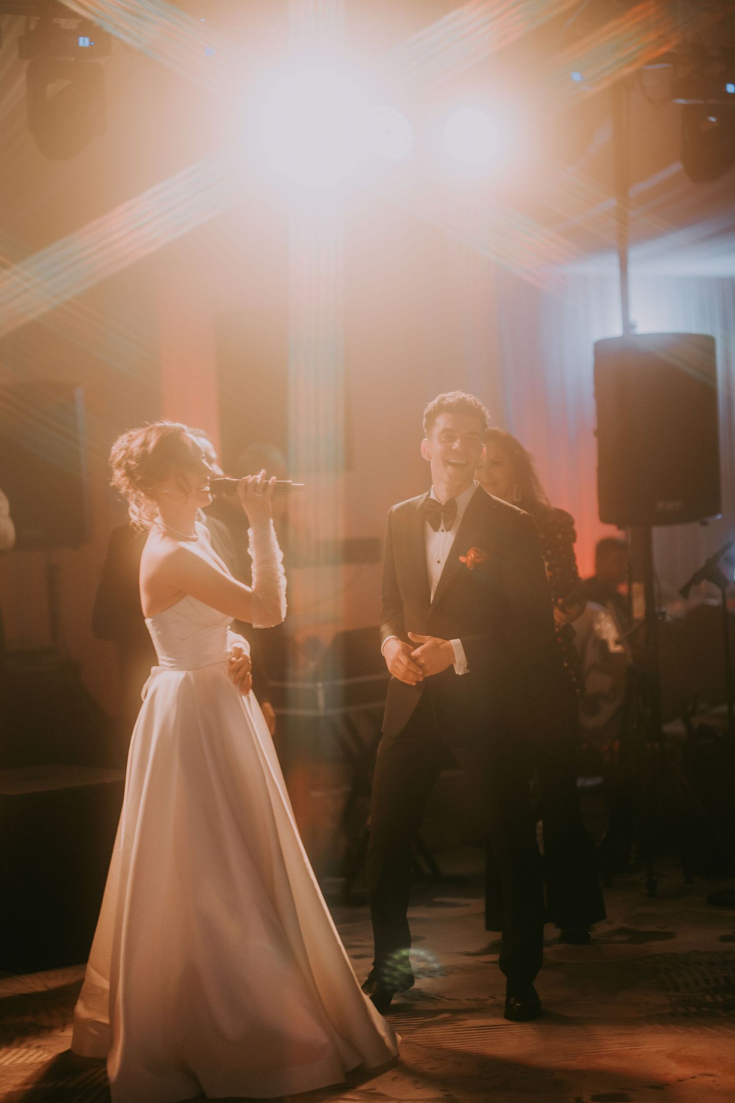 Bride singing into microphone for groom during first dance under warm spotlights at wedding reception. Epicu Fotograf Drobeta-Turnu Severin