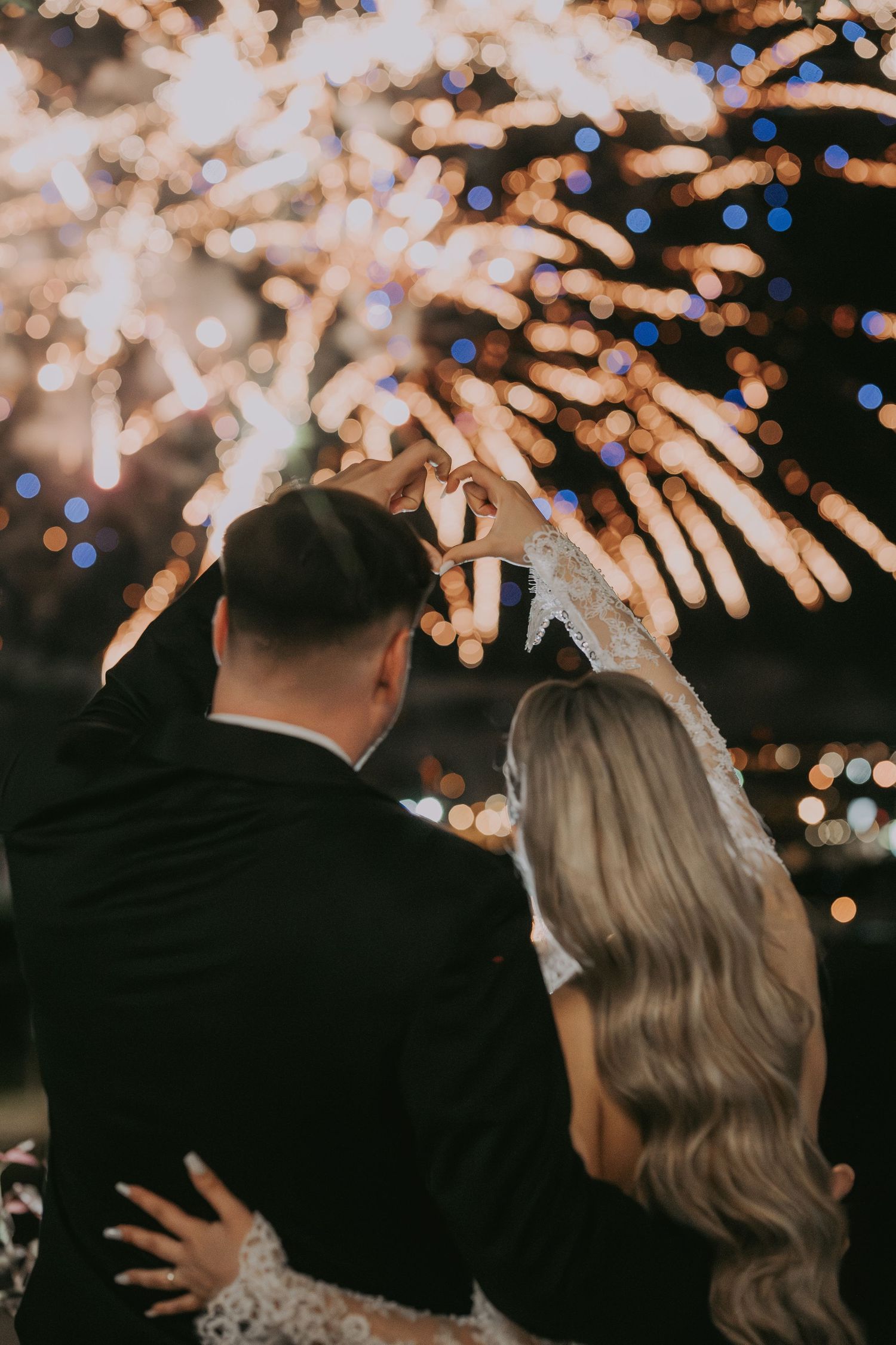 Newlyweds embrace while watching a stunning fireworks display light up the night sky.