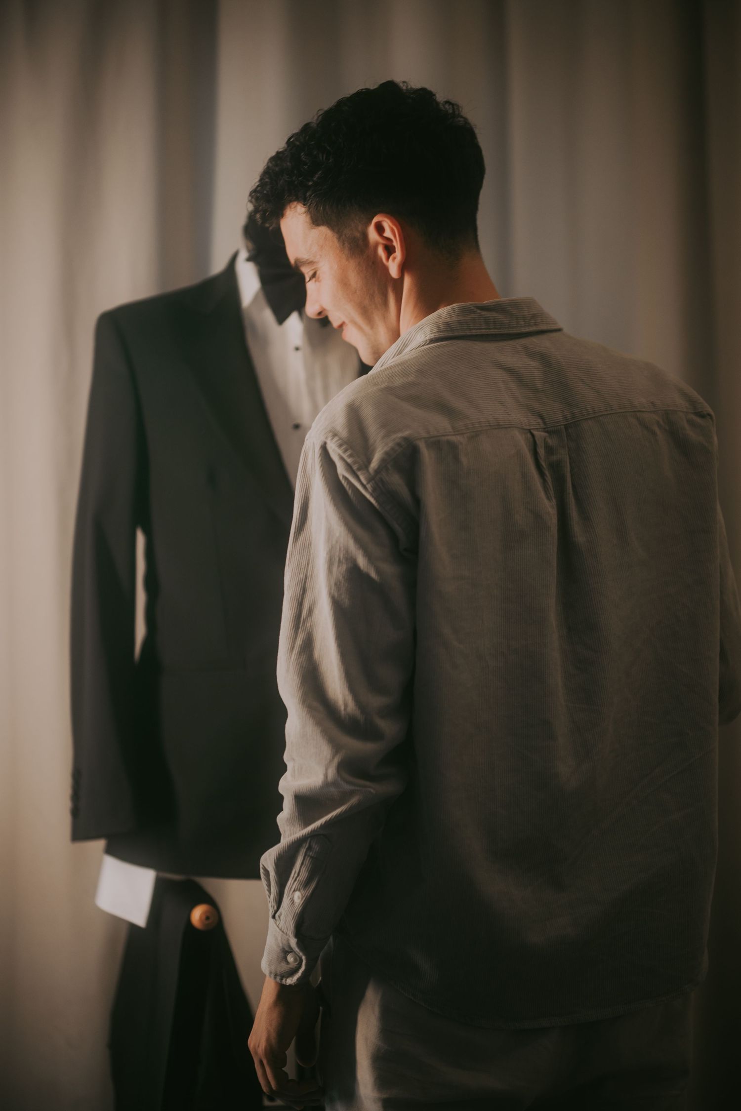 Young man in gray shirt examining a black suit on a mannequin in soft natural light. Epicu Fotograf Drobeta-Turnu Severin