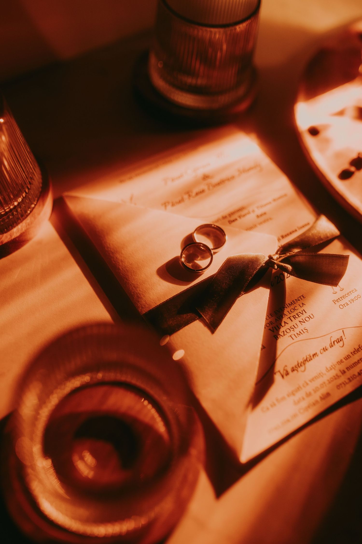 Gold-toned wedding invitation with two rings and ribbon bow in warm romantic lighting. Epicu Fotograf Drobeta-Turnu Severin