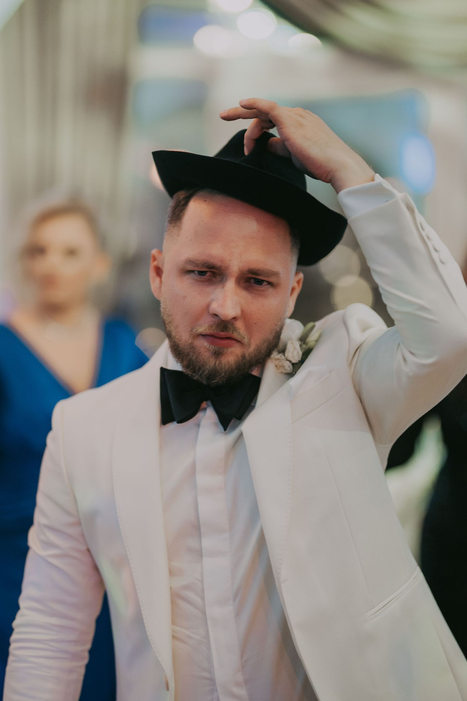 Stylish groom in white tuxedo and black bow tie adjusting his black fedora hat at wedding. Epicu Fotograf Drobeta-Turnu Severin