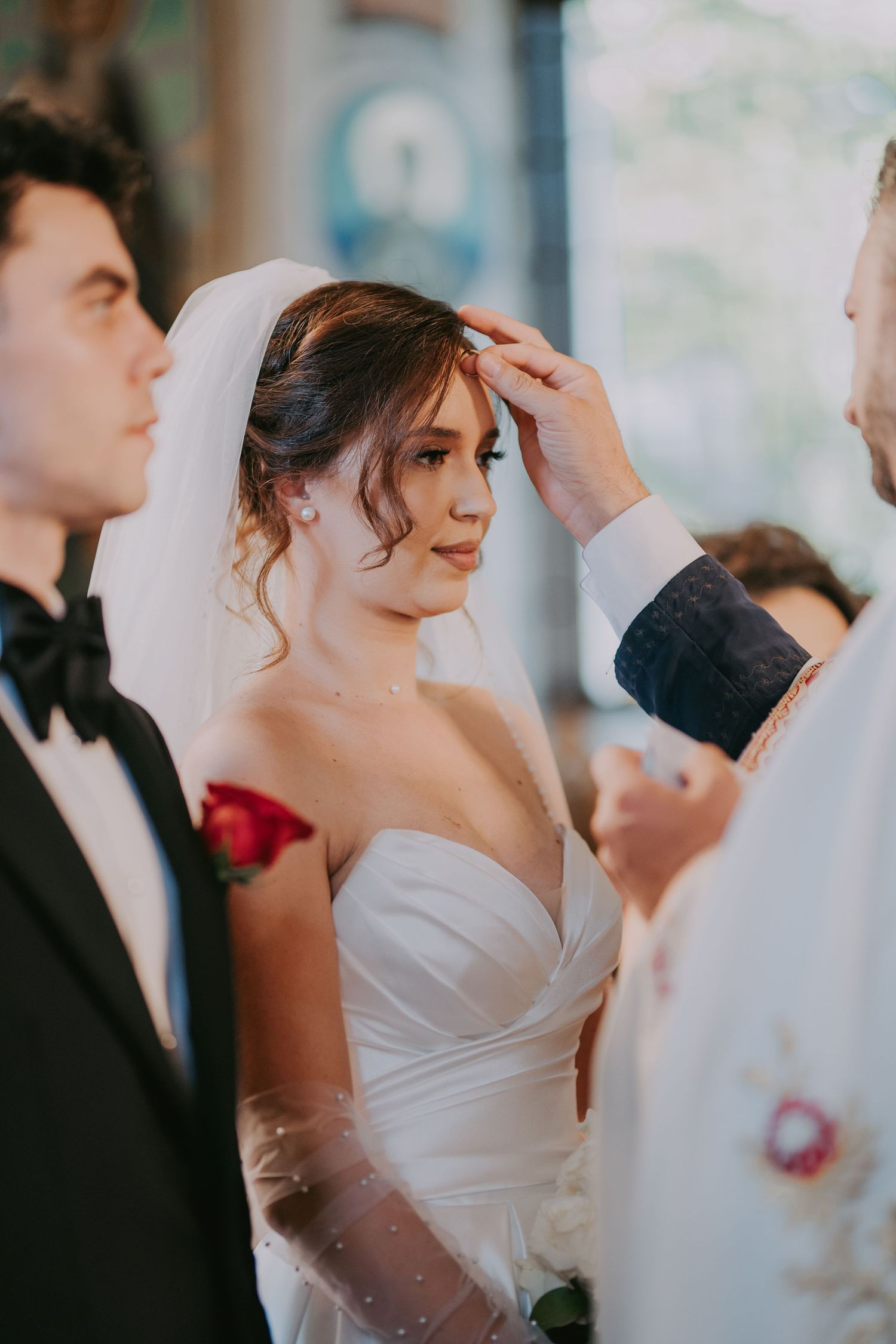 Bride in strapless white gown receives blessing from priest during Orthodox church wedding ceremony. Epicu Fotograf Drobeta-Turnu Severin