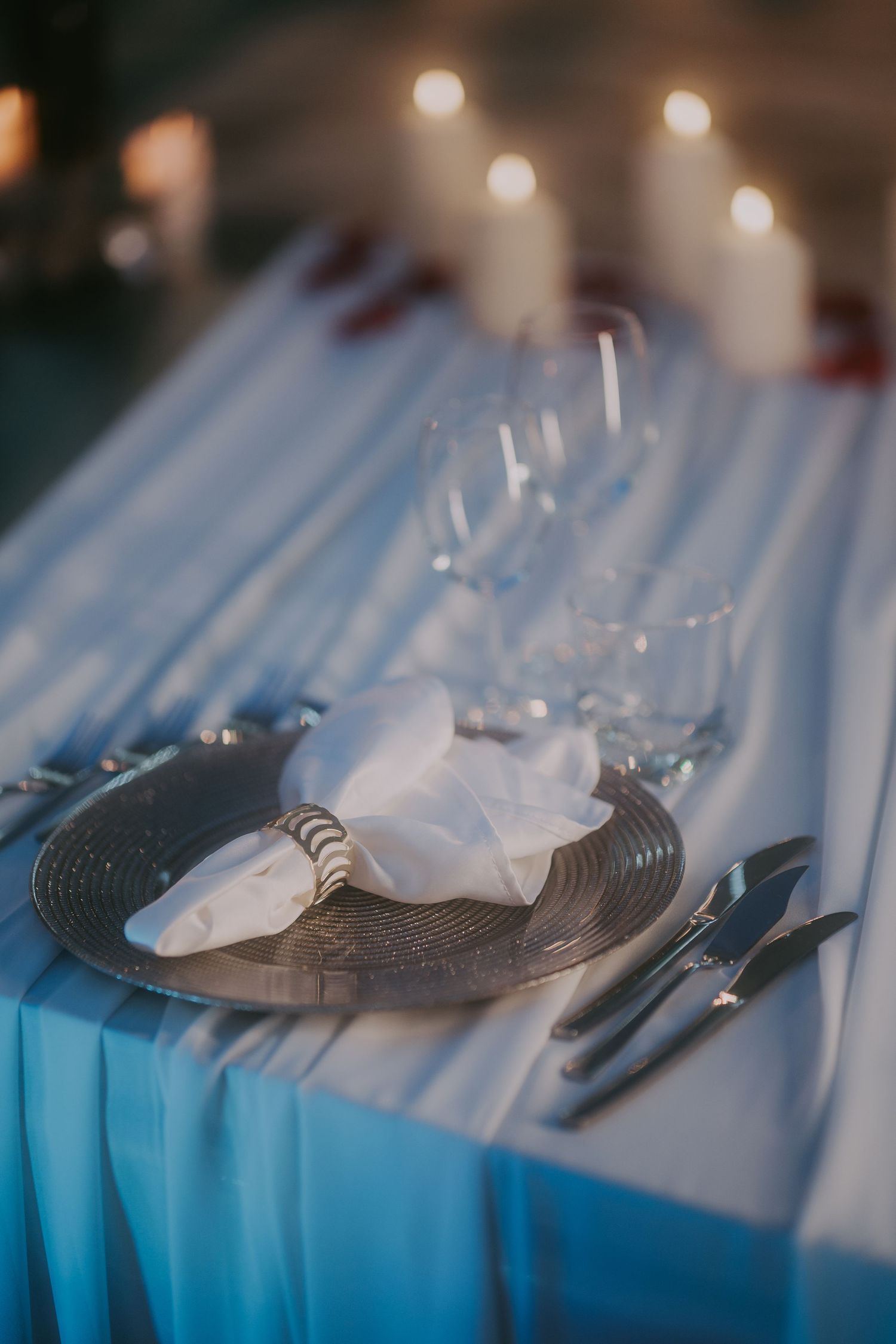 Elegant wedding place setting with silver charger plate, white napkin, and glowing candles. Epicu Fotograf Drobeta-Turnu Severin