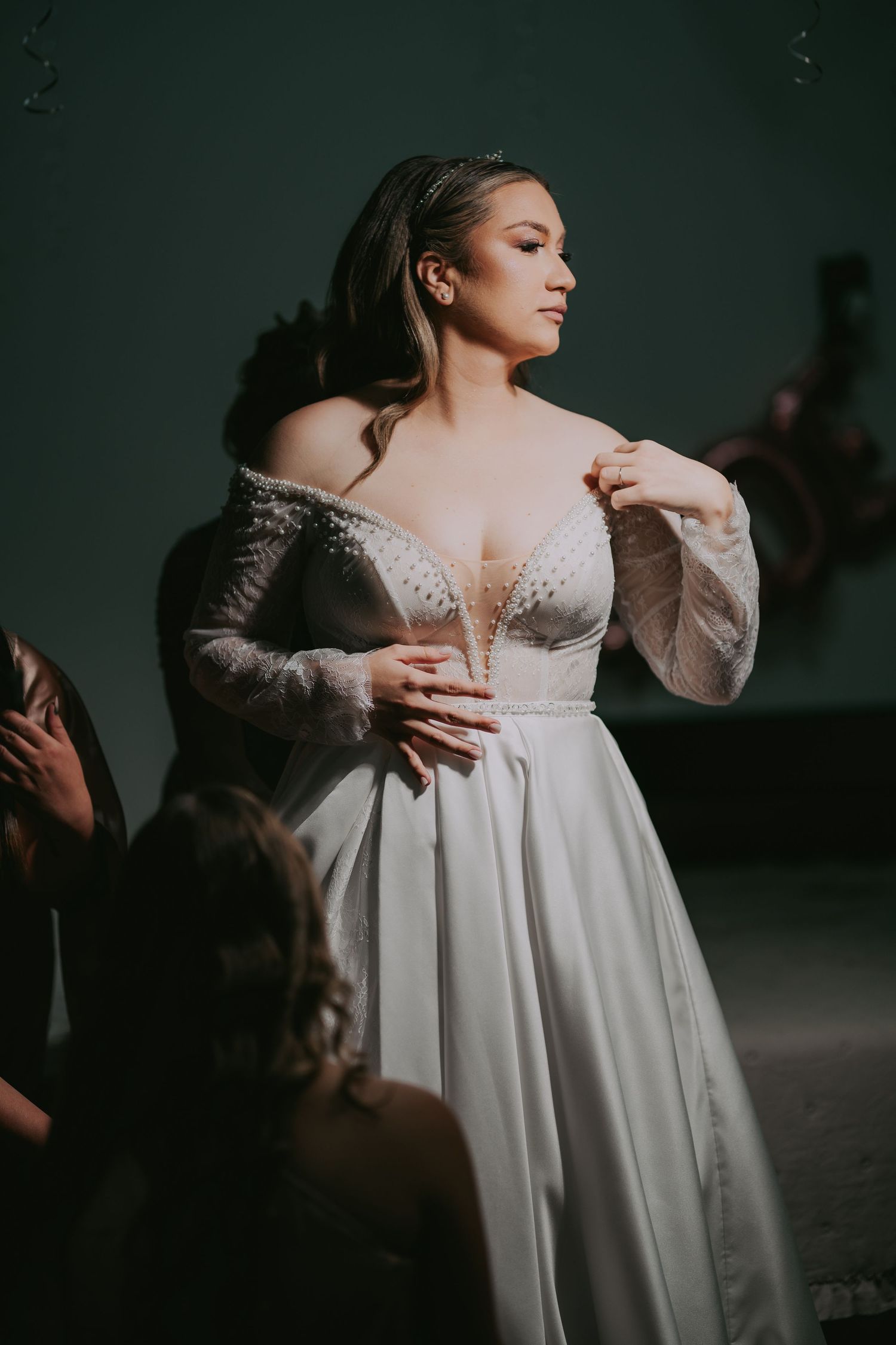 Bride being helped into an elegant off-shoulder beaded wedding gown by bridesmaids in a moody setting. Epicu Fotograf Drobeta-Turnu Severin