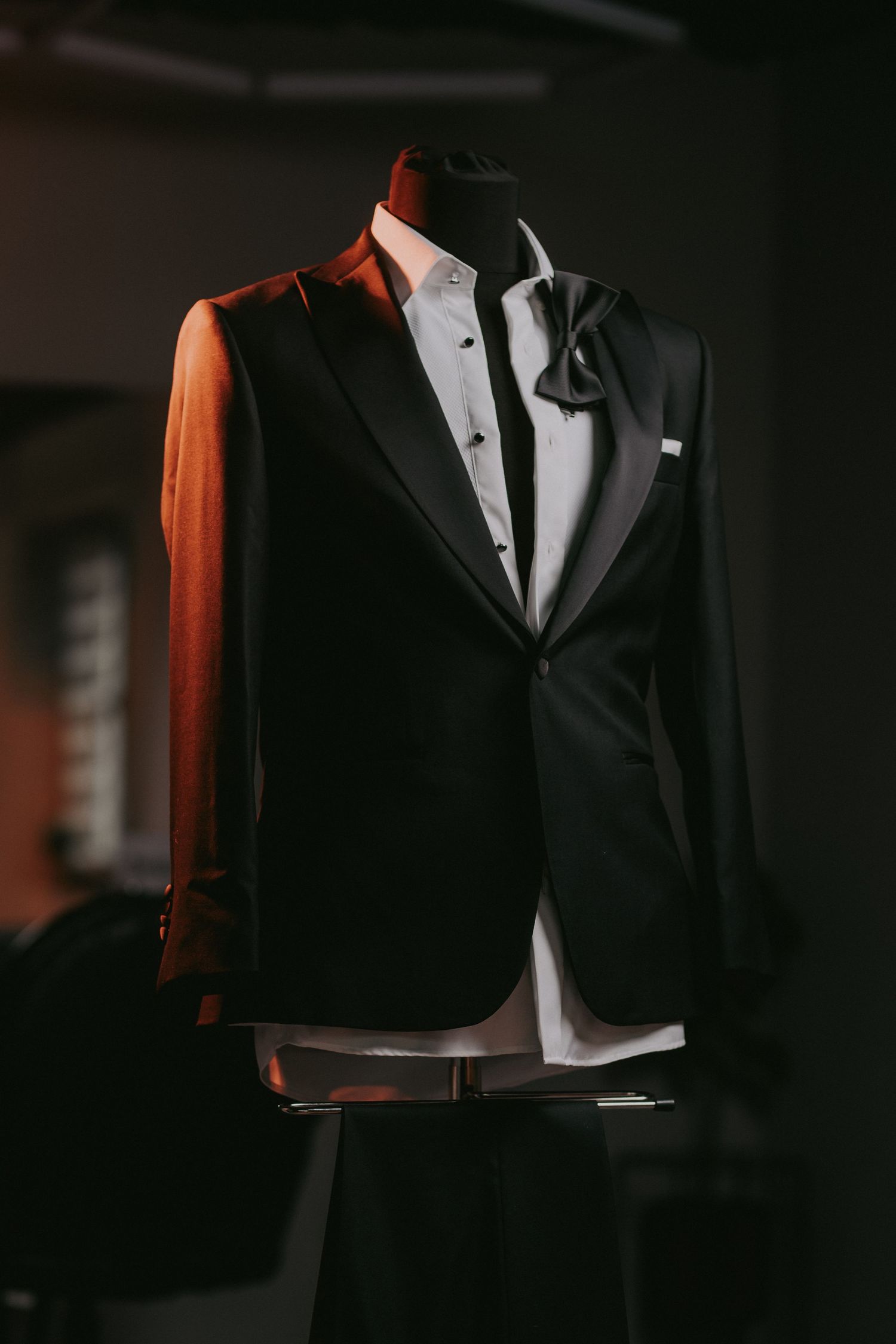 Classic black tuxedo with bow tie displayed on a mannequin in dramatic dark studio lighting.