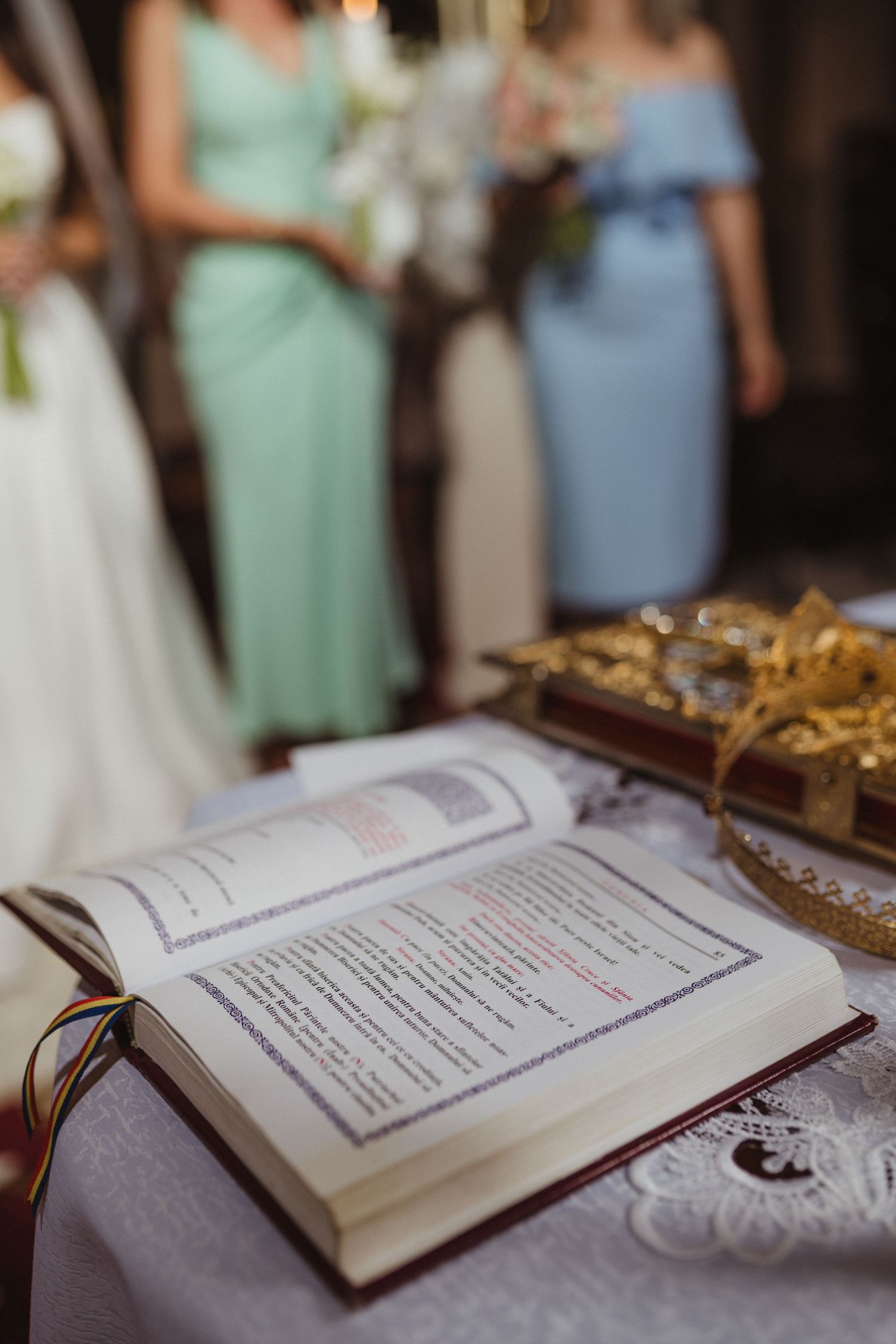 Open Orthodox wedding ceremony book on a lace-covered altar table with golden crowns beside bridesmaids in mint dresses.