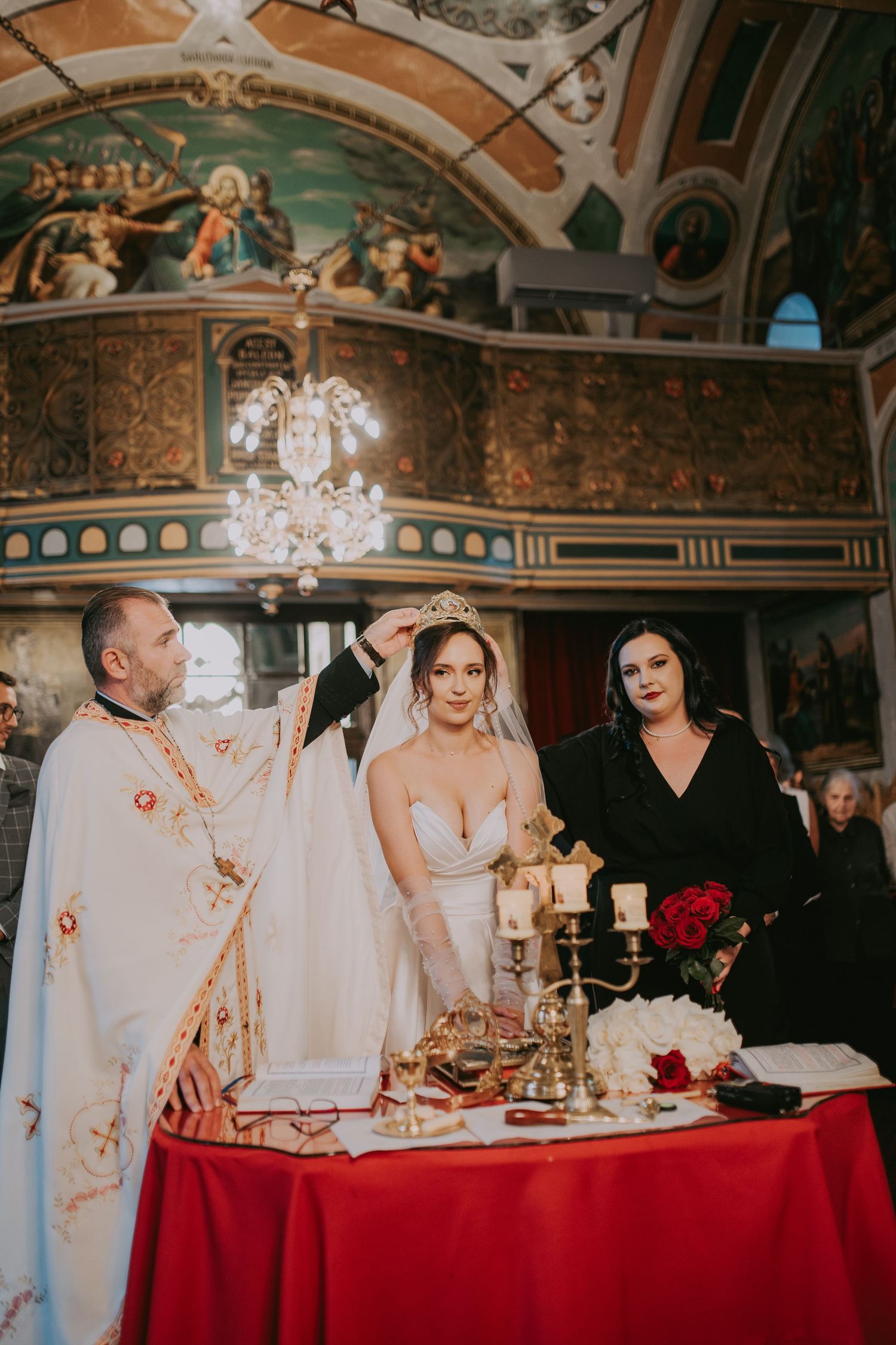 Orthodox priest crowning bride during traditional wedding ceremony at candlelit red altar. Epicu Fotograf Drobeta-Turnu Severin