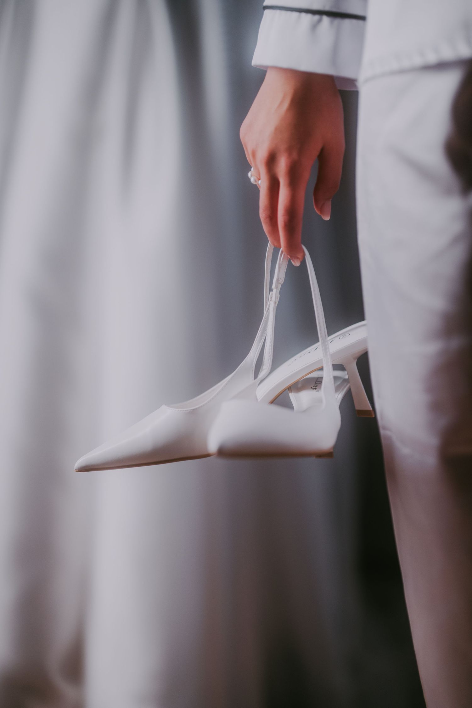 Bride holding elegant white pointed-toe satin heels with ribbon straps in her hand. Epicu Fotograf Drobeta-Turnu Severin